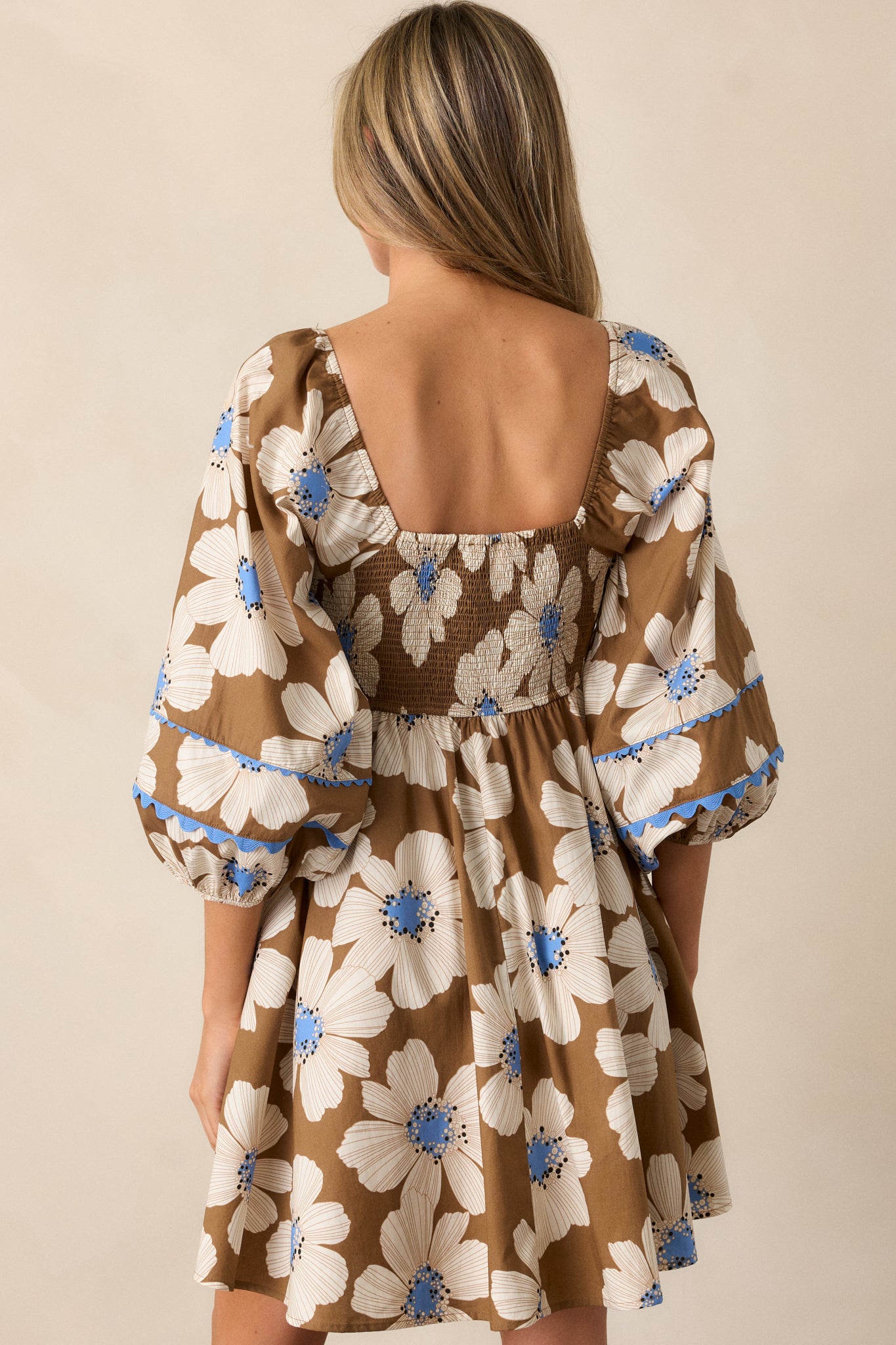 Back view of the camel brown dress, showcasing the smocked back insert and puff sleeve details. The blue ric rac trim along the back hem and sleeve cuffs is also visible.