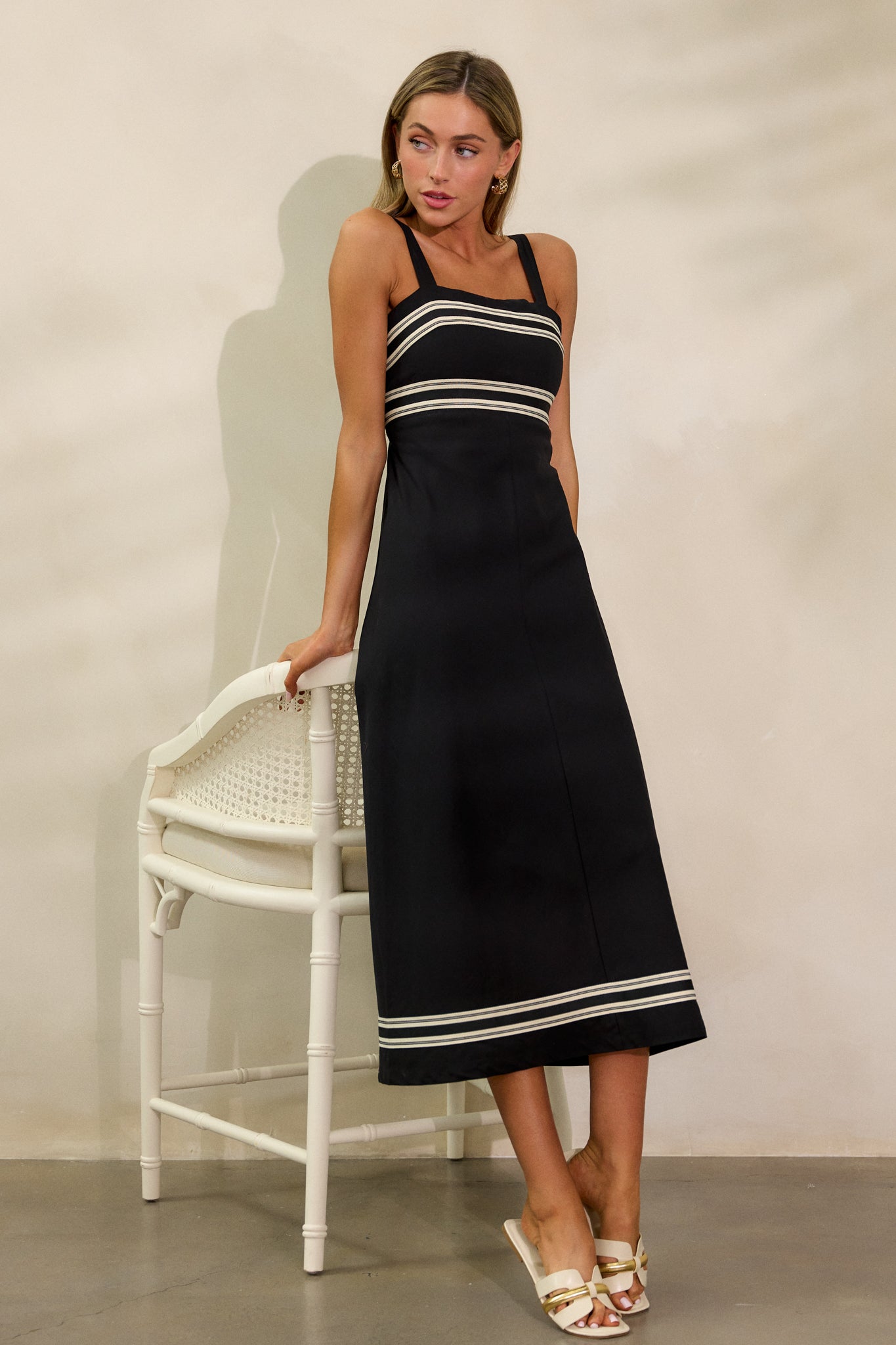 Full front view of the black dress, showcasing its straight neckline, midi length, and contrast detailing around the bust, waist, and bottom hem.