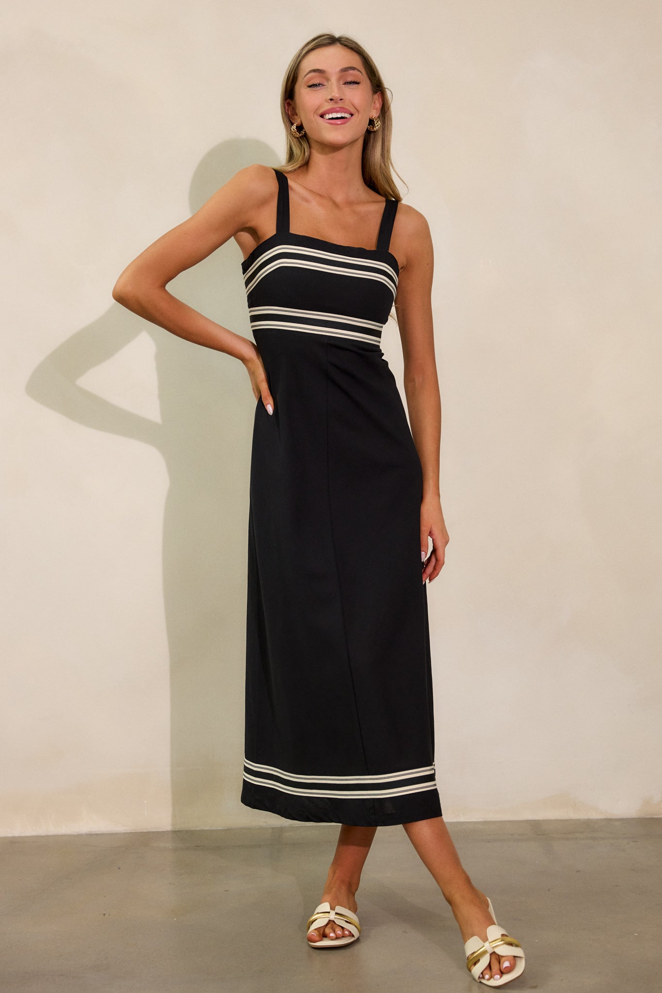 Full length view of the black dress, emphasizing the adjustable wide straps and the clean, elegant lines of the dress.