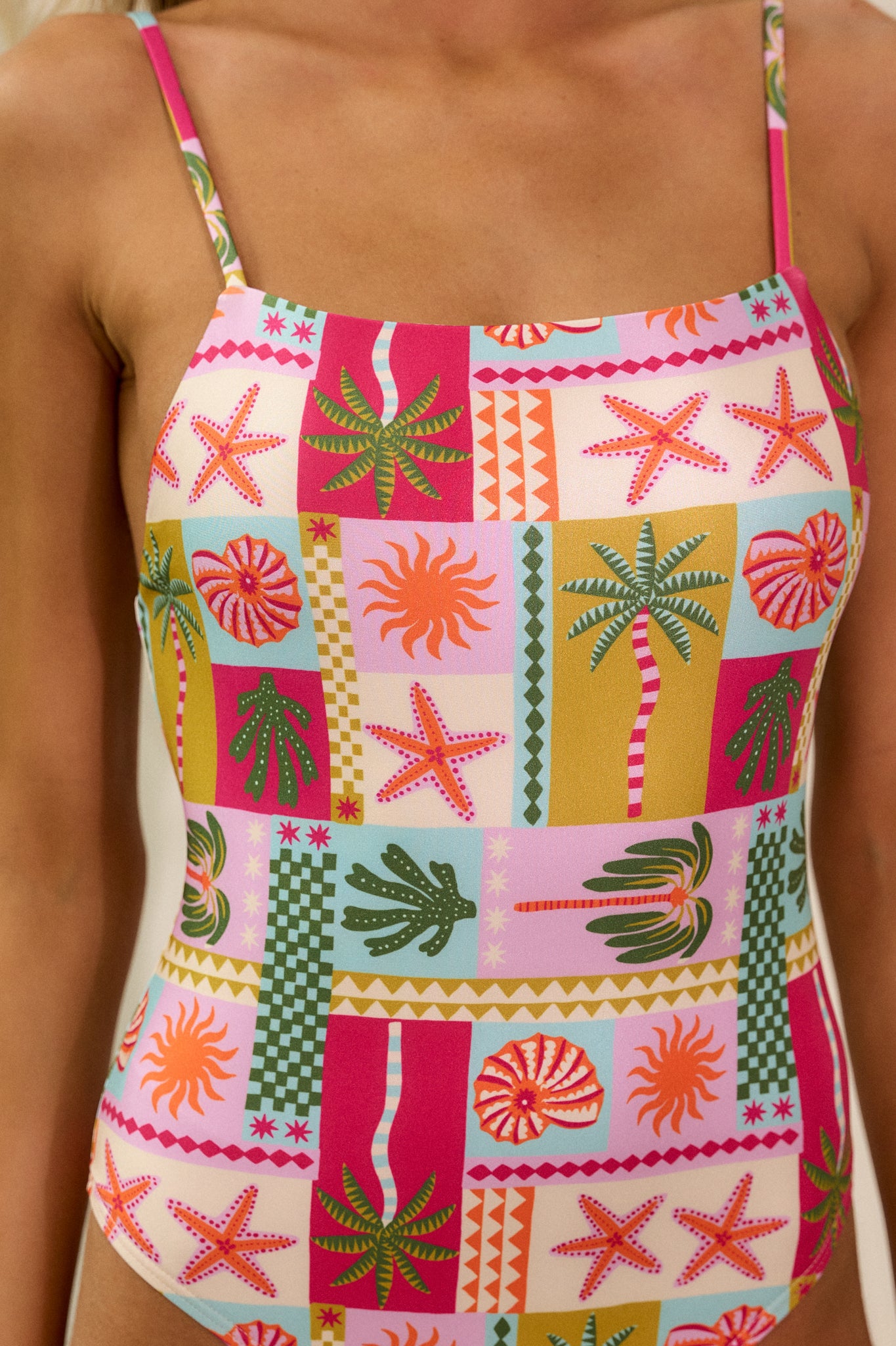 Close-up of the tropical print on the pink one-piece swimsuit, showing the vibrant colors and pattern along with the fabric texture.