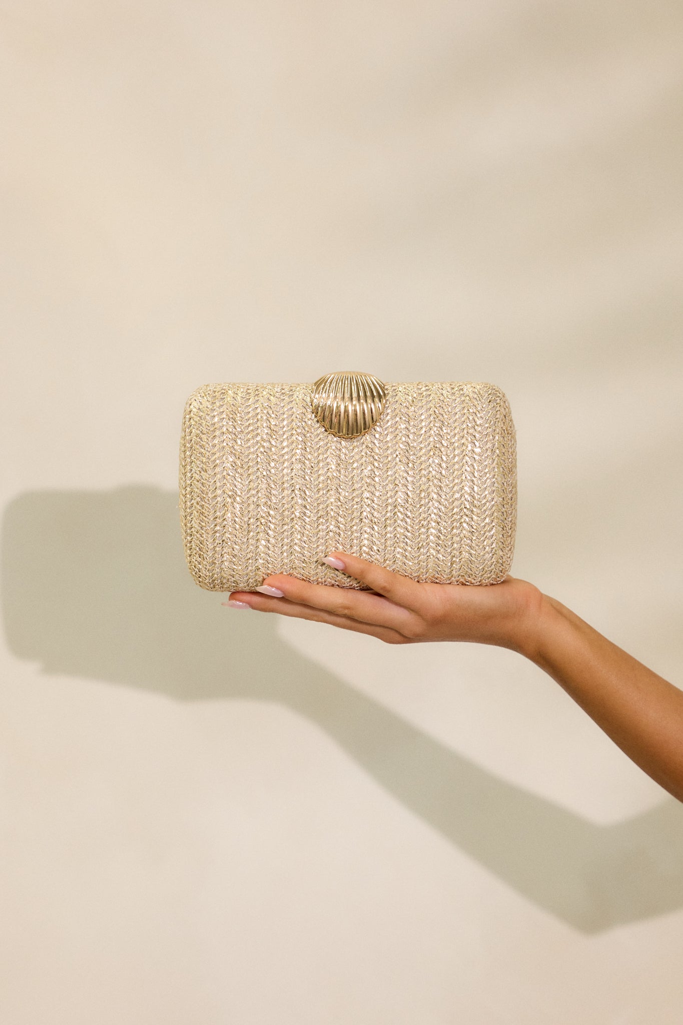 A full view of the gold woven clutch, featuring its seashell snap closure, gold hardware, and the optional crossbody chain.