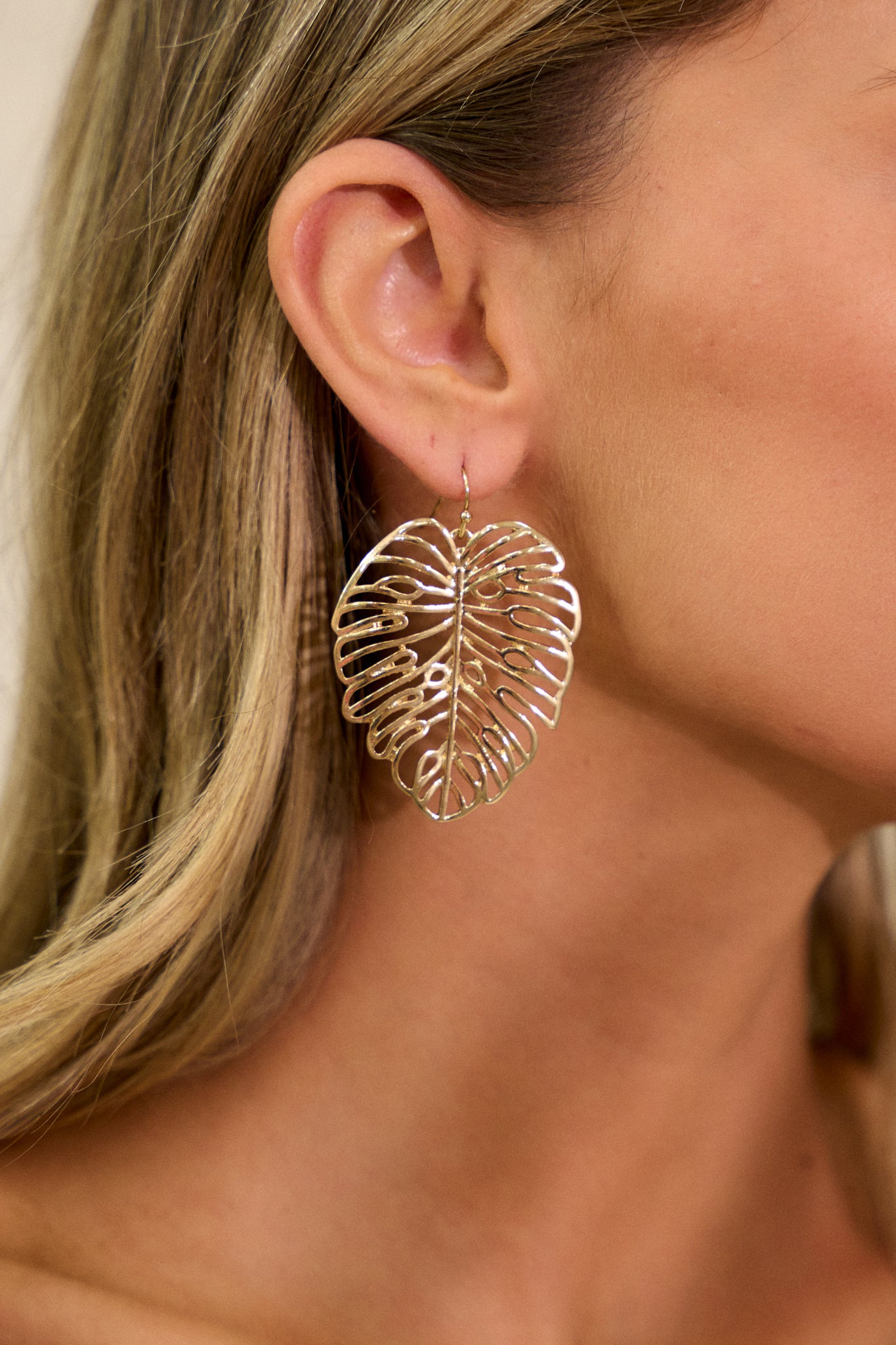 Detailed shot of the gold earrings, focusing on the transparent monstera leaf dangles and the fine gold hardware. The earrings add a natural touch to any look.