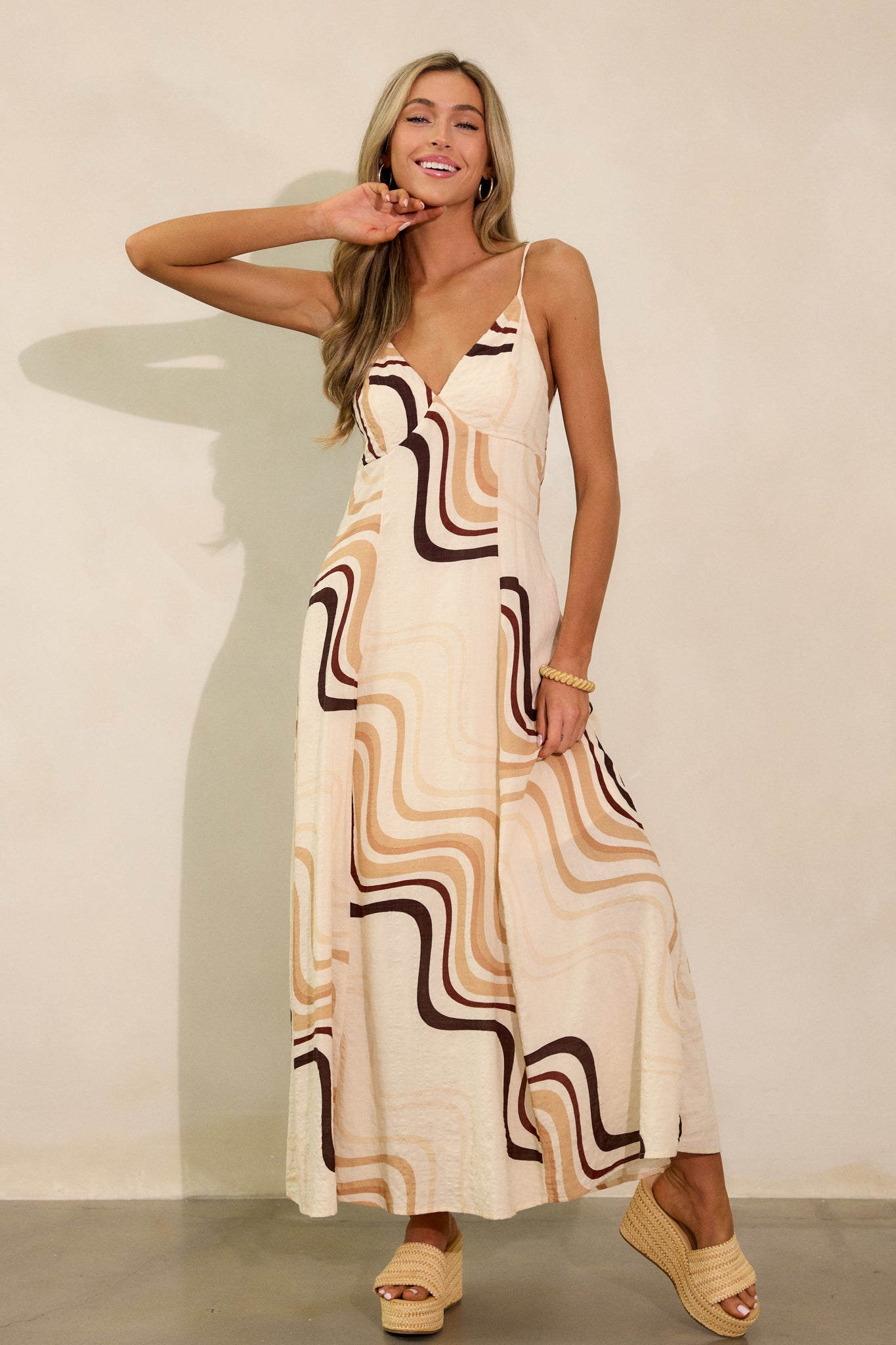 A complete shot of the beige maxi dress with a plunging v-neckline, tie back, and functional hip pockets, showcasing its fun and unique print.