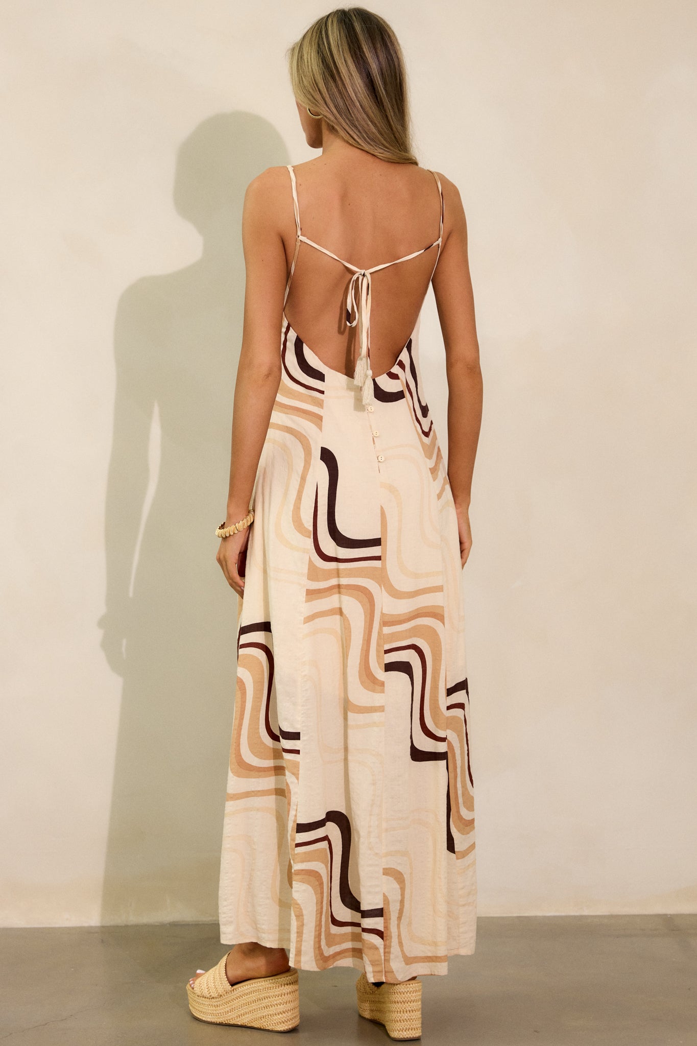 Back view of the beige maxi dress, focusing on the tie back and row of buttons running down the spine, with the dress’s unique print visible.