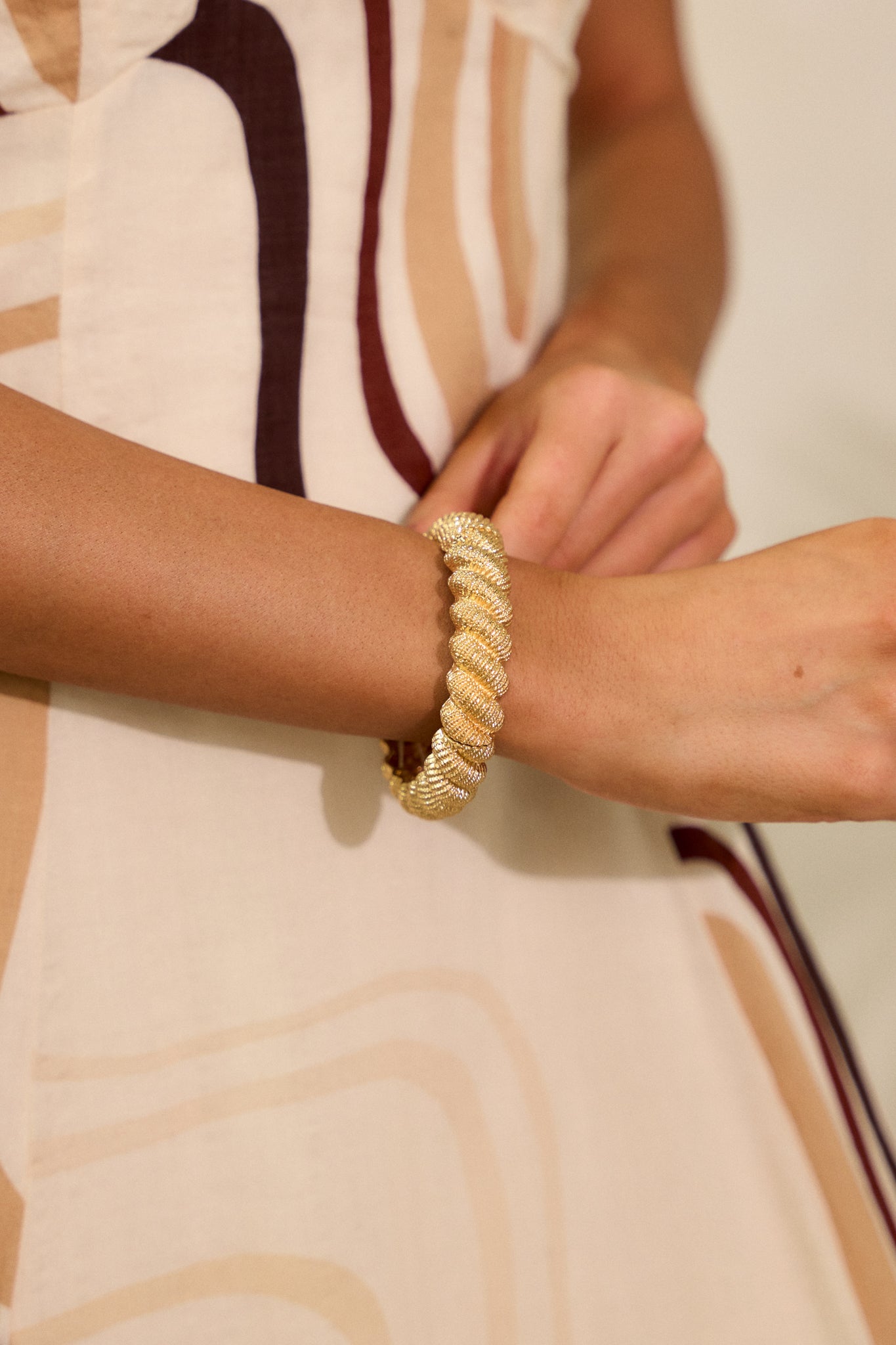 A cropped shot of the gold bracelet, highlighting the textured rope design. The bracelet's gold hardware is visible, showcasing its intricate texture against the smooth surface of the bracelet.