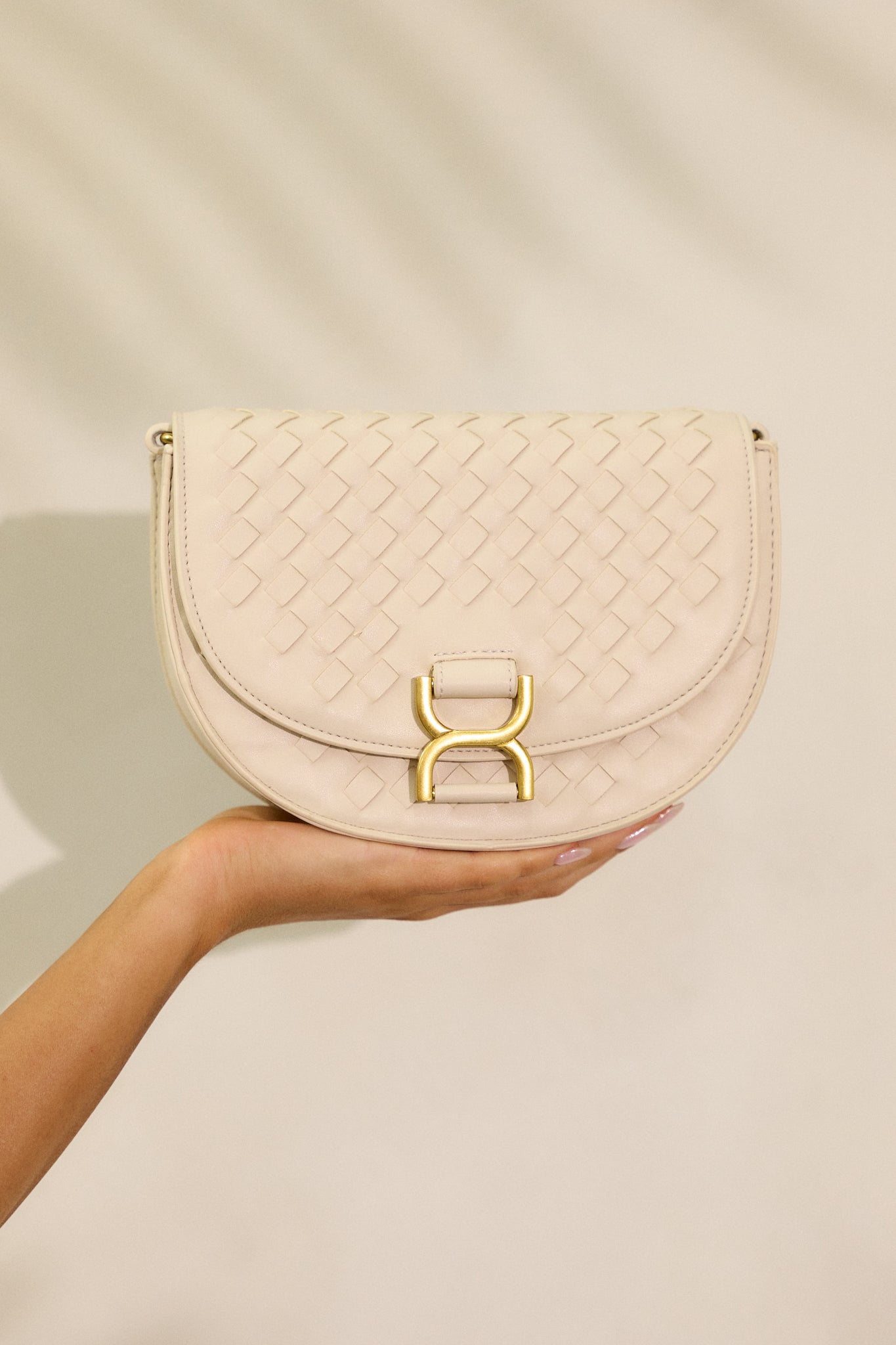 A close view of the beige woven texture of the faux leather handbag, focusing on the gold buckle snap closure and the elegant fold-over design.