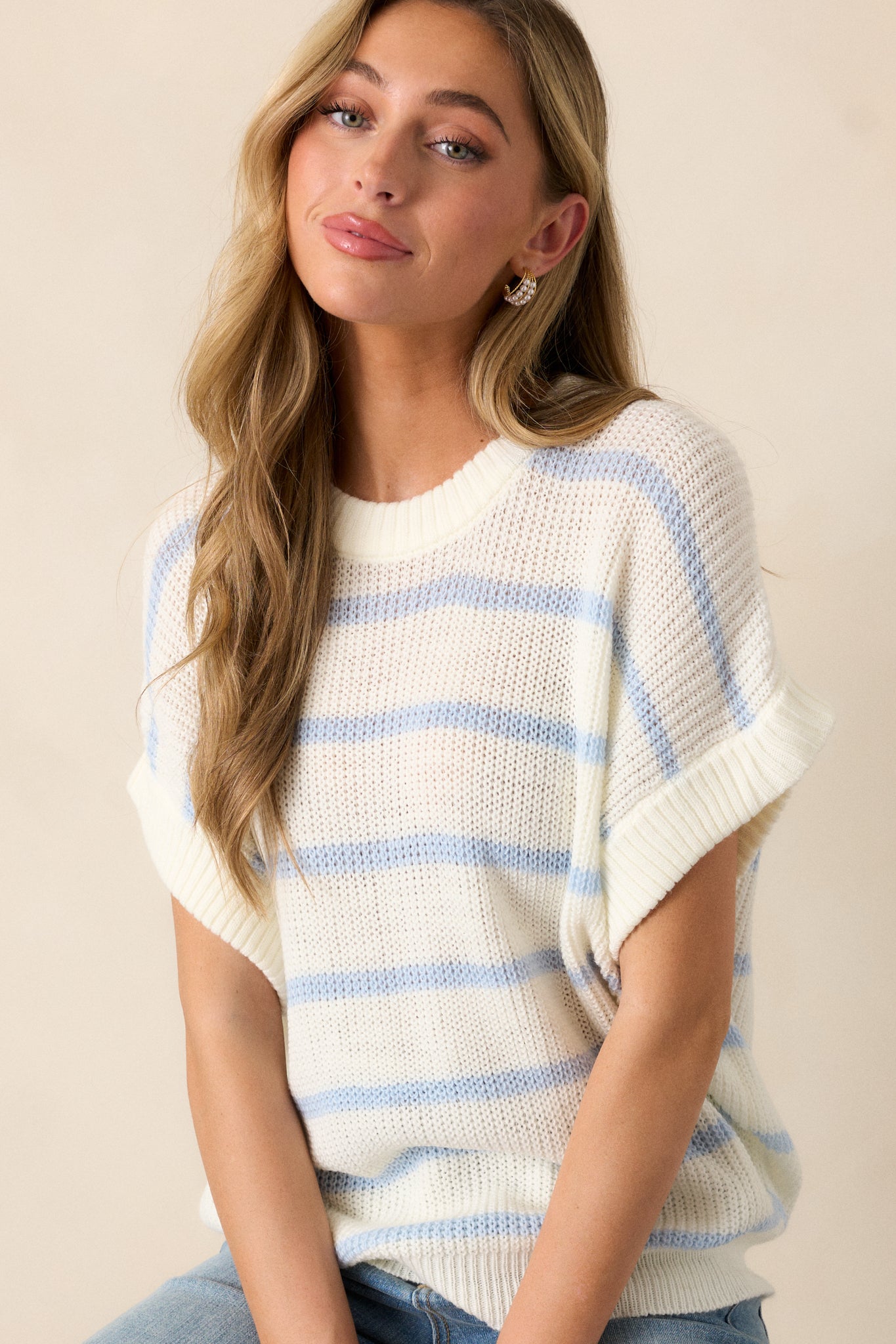 A cropped image emphasizing the short oversized sleeves of the white sweater. The ribbed detailing at the neckline and bottom hem is visible, with the striped pattern adding a touch of flair.