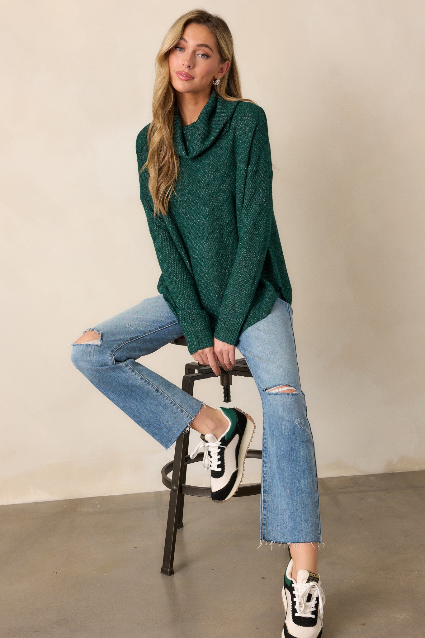 A full-length view of a hunter green sweater featuring a cowl turtleneck, scooped hemline, and speckled coloring.