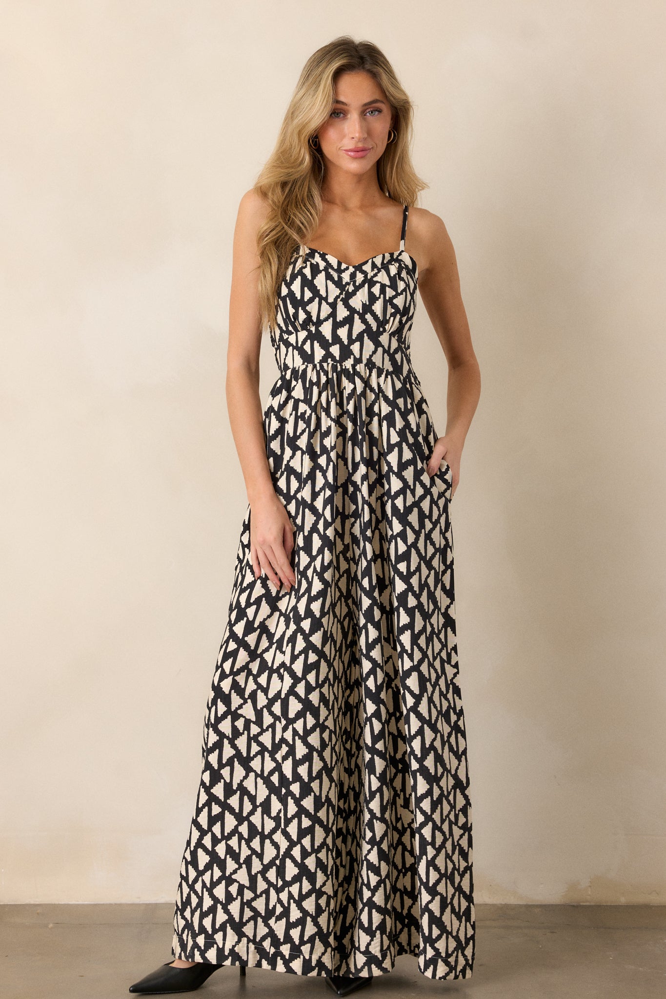 A black jumpsuit with a slight sweetheart neckline, geometric print, and wide-leg pants is shown in a full-body front view.