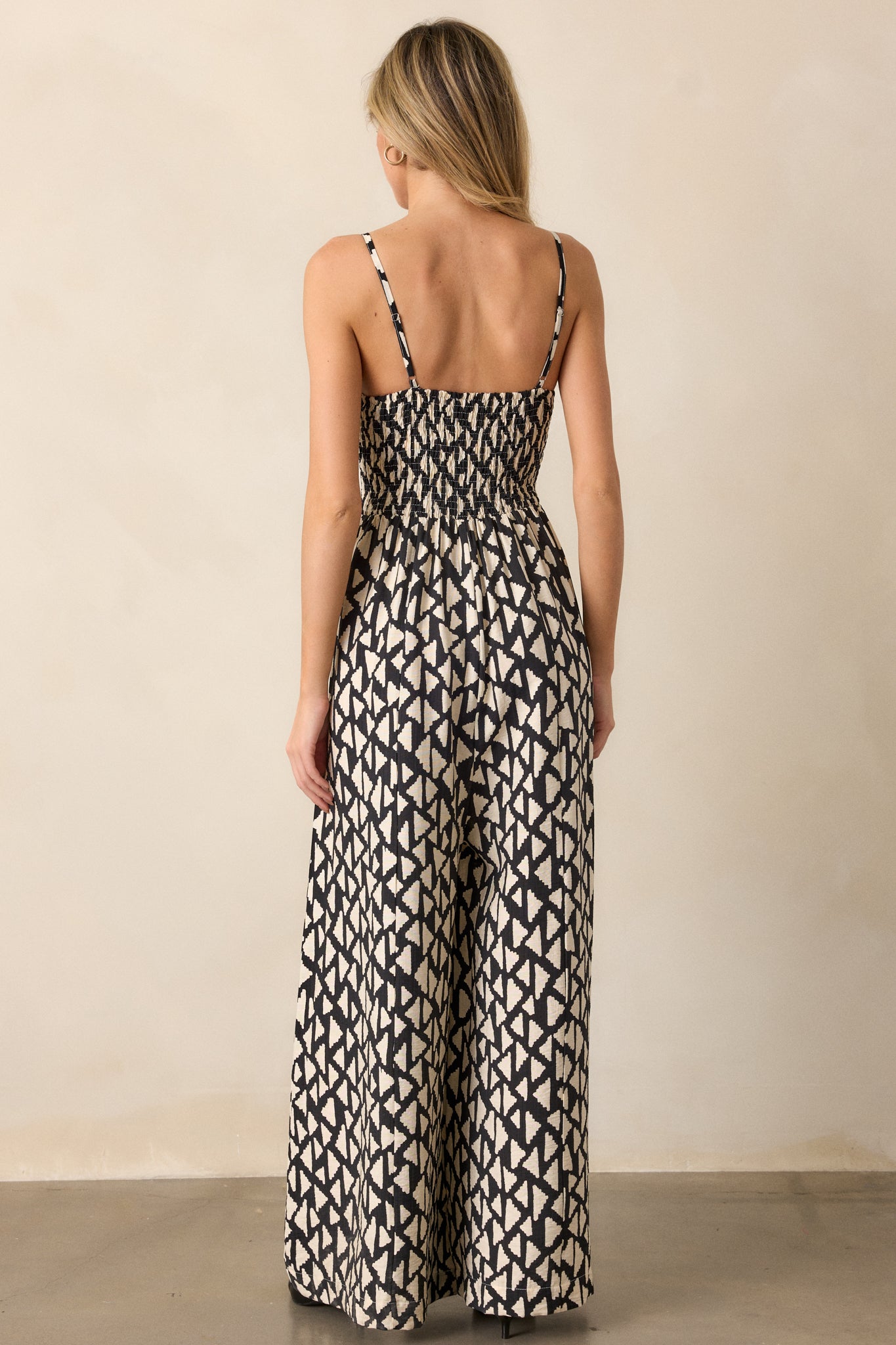 A rear view of the black jumpsuit highlighting the smocked back panel, adjustable straps, and flowing wide-leg pants.