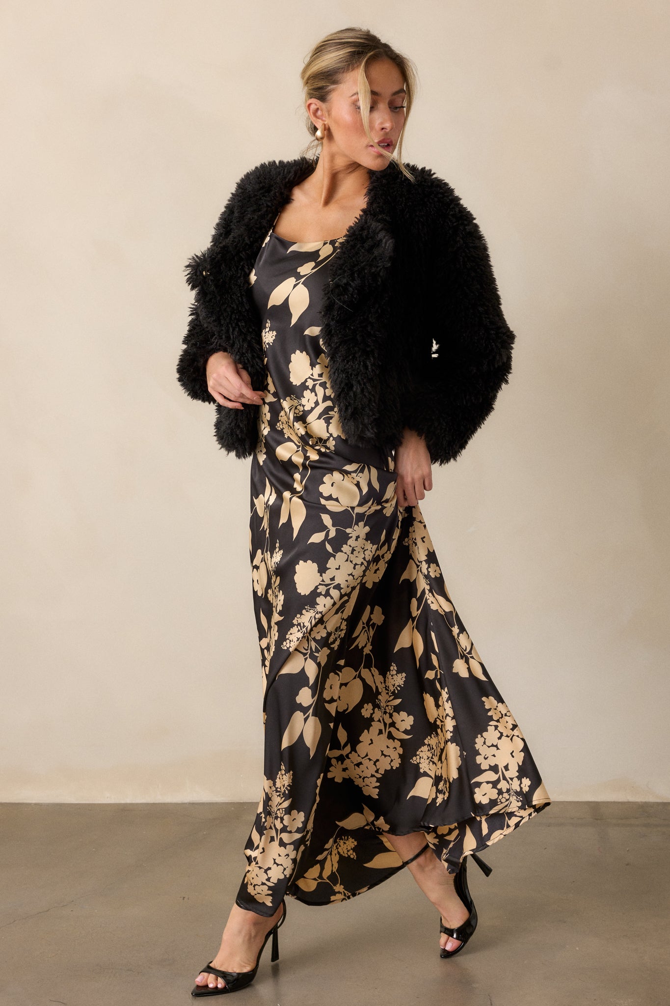 A full view of the black dress, showcasing the bold black and gold floral design, sleeveless cut, and flowing maxi length.