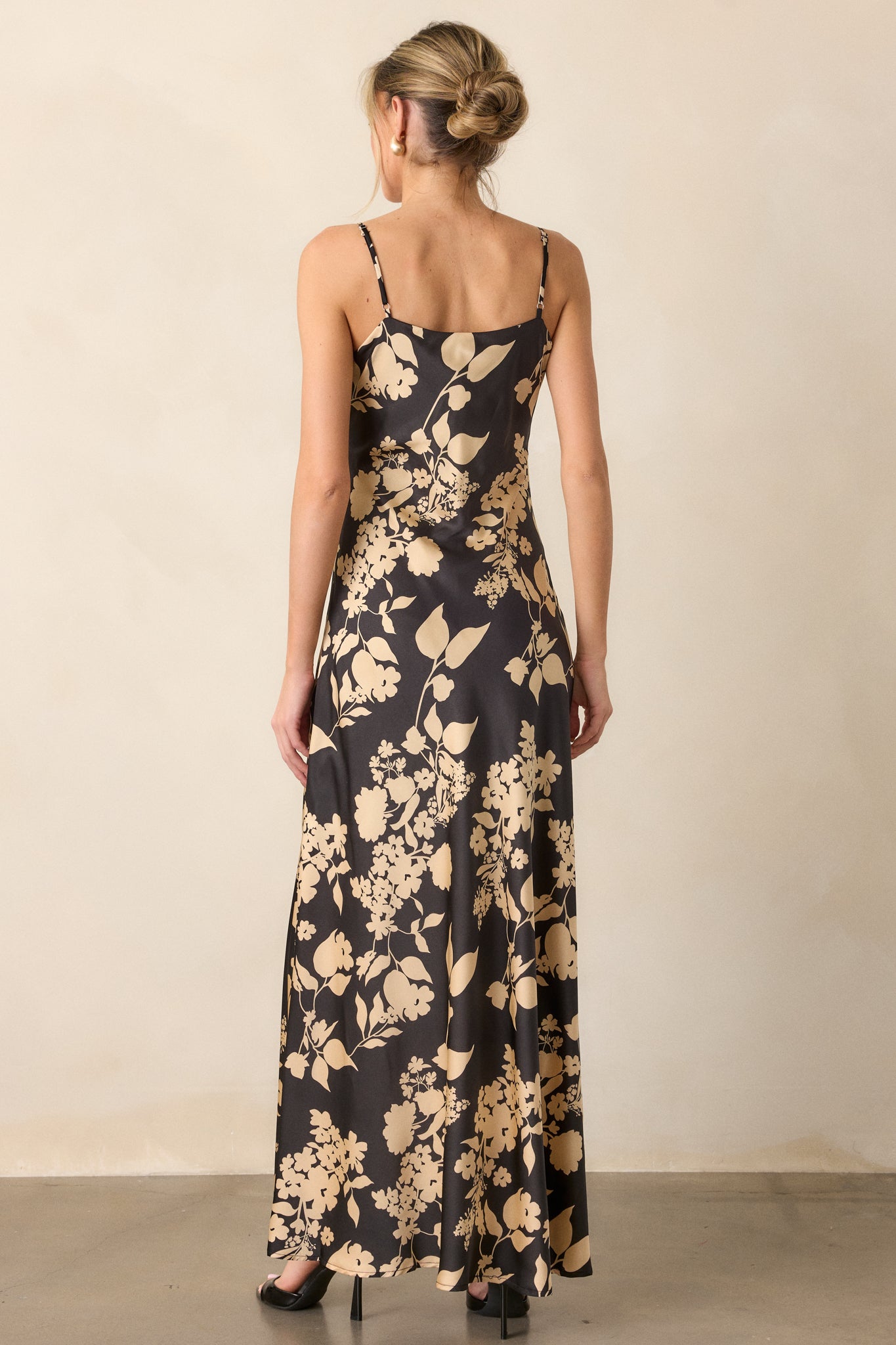 View of the back of the dress, featuring the continuous bold black and gold floral design flowing down the entire maxi length.