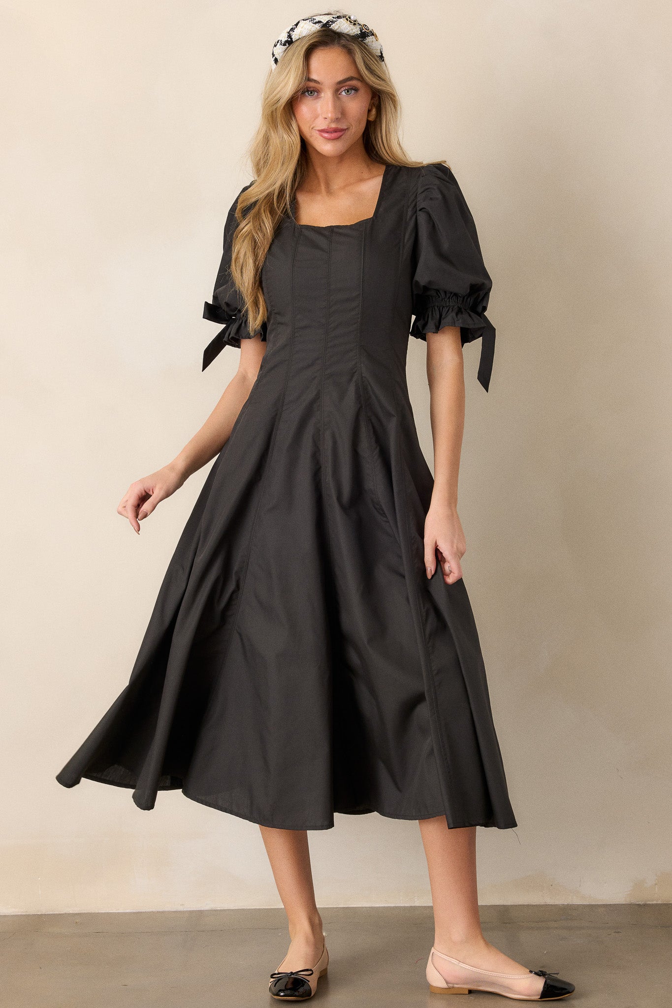 A front view of the black dress, focusing on the puff sleeves with bow accents and the soft, flaring midi-length hem.