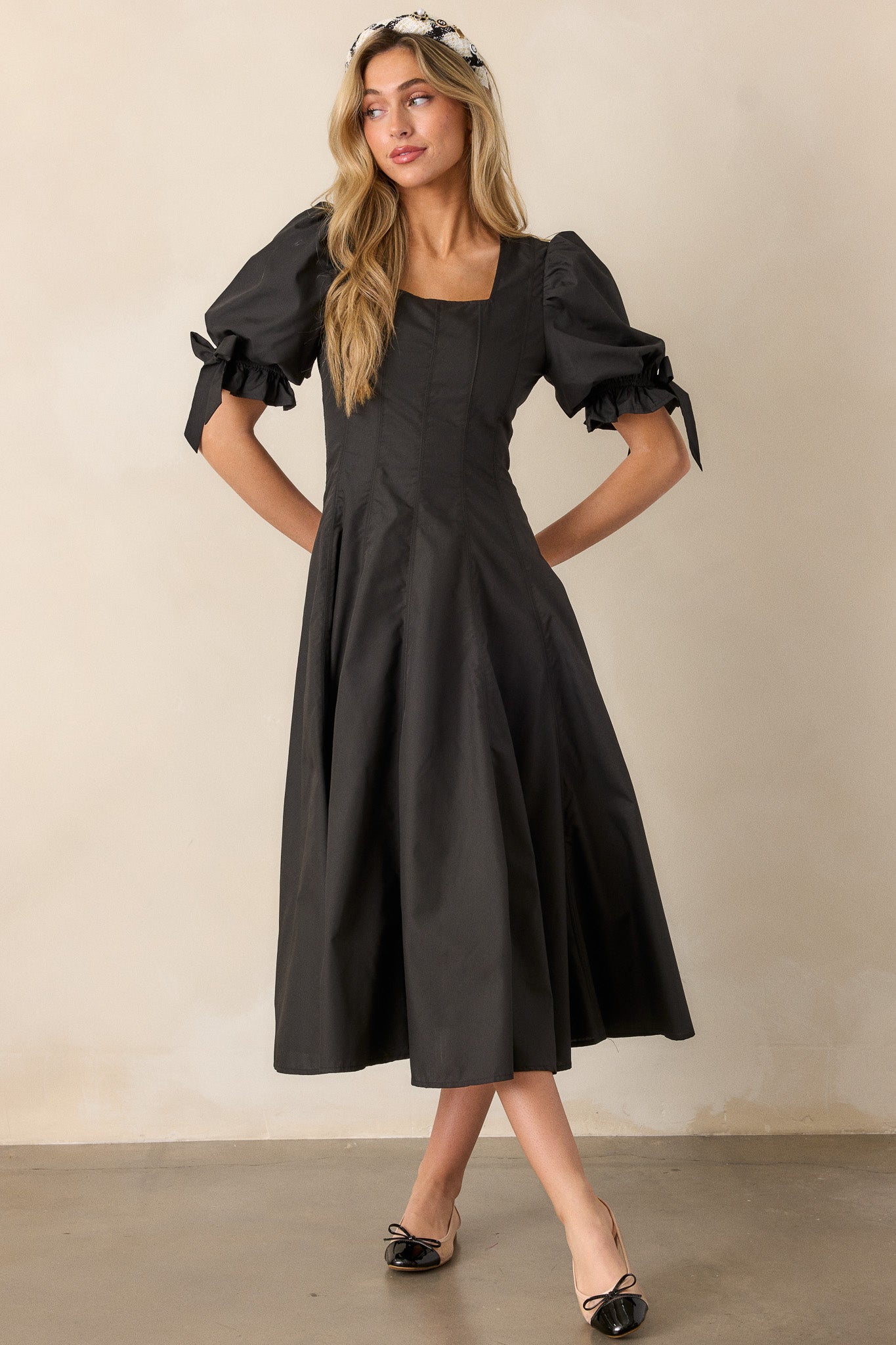 A front-facing view of the black dress, highlighting the fit-and-flare design, square neckline, and the puff sleeves with bow details.