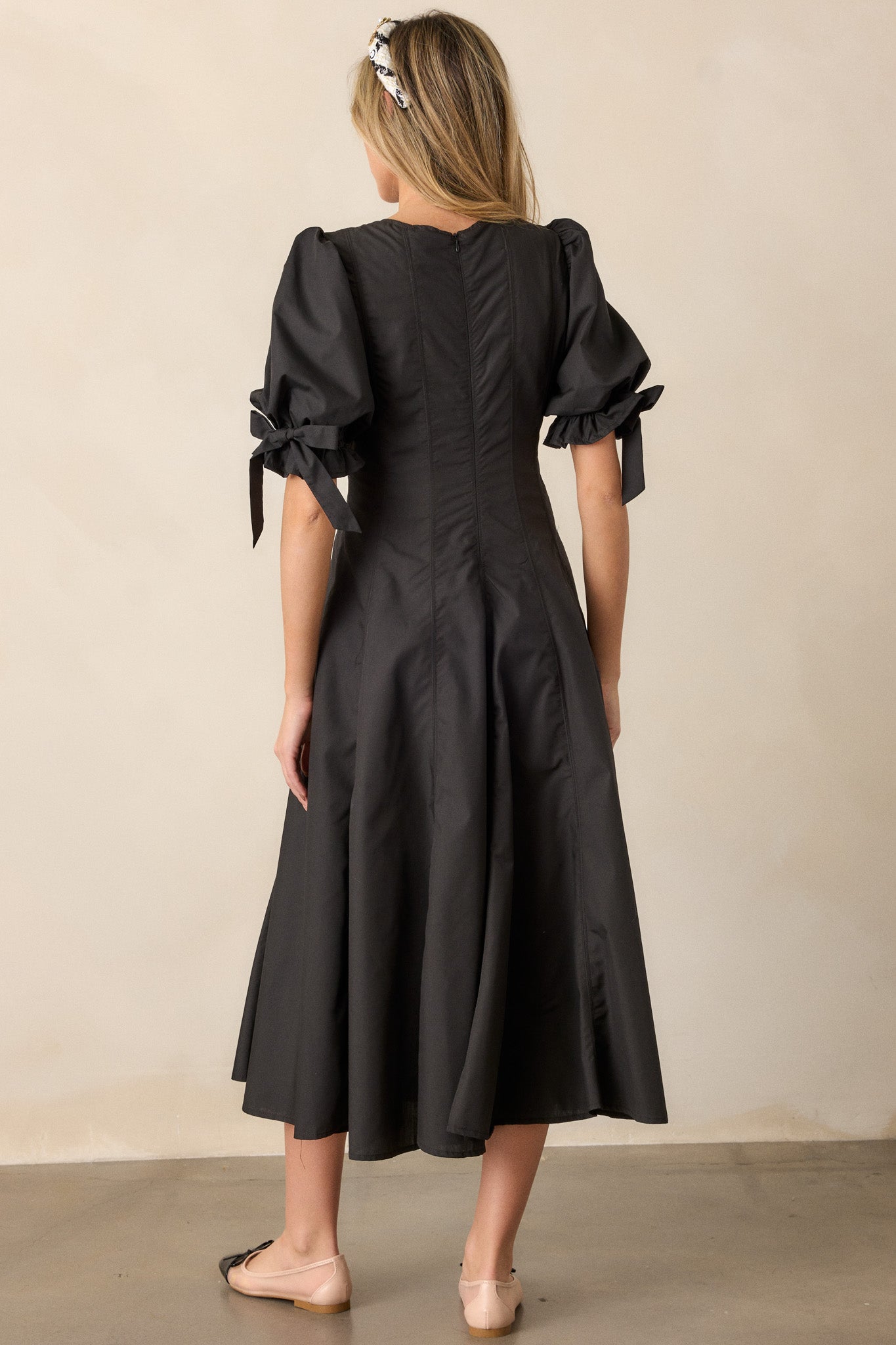 A back view of the black dress, showcasing the discrete back zipper and vertical seam details running down the dress.