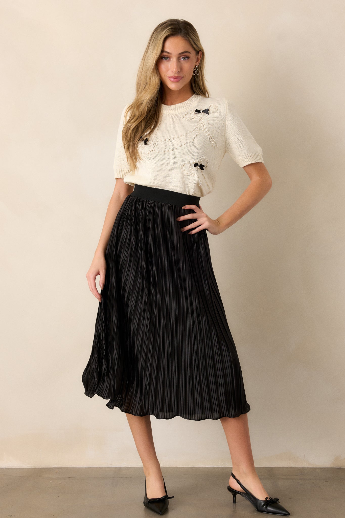 Full view of a black skirt featuring a high-waisted fit, showcasing its pleated design and shiny material in a stylish setting.