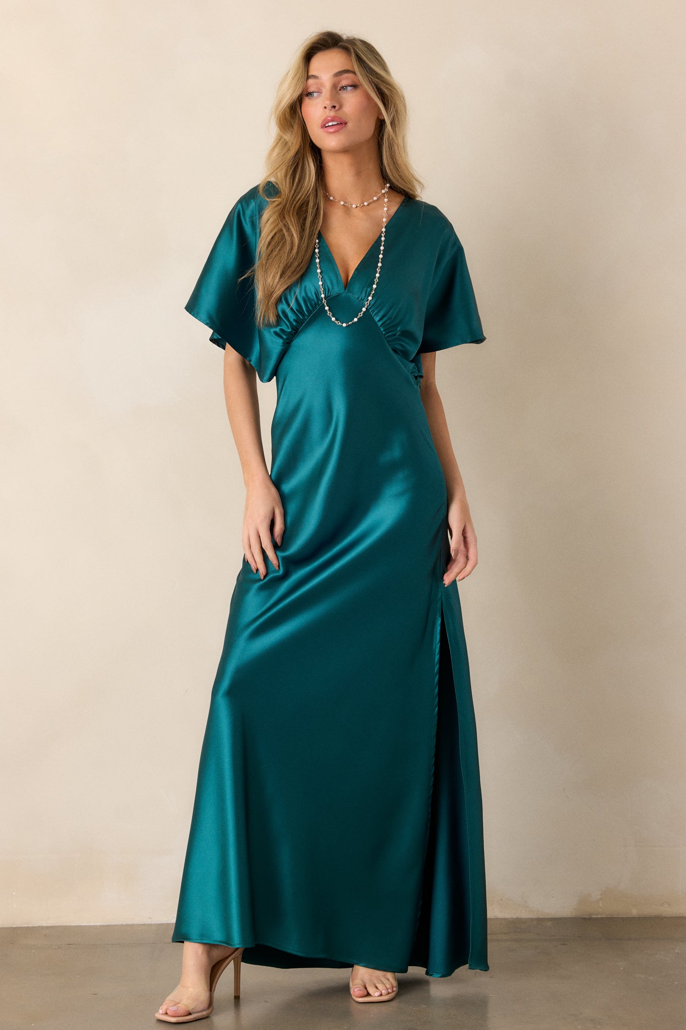 A full-length view of a teal satin dress featuring a deep V-neckline and kimono-style sleeves.