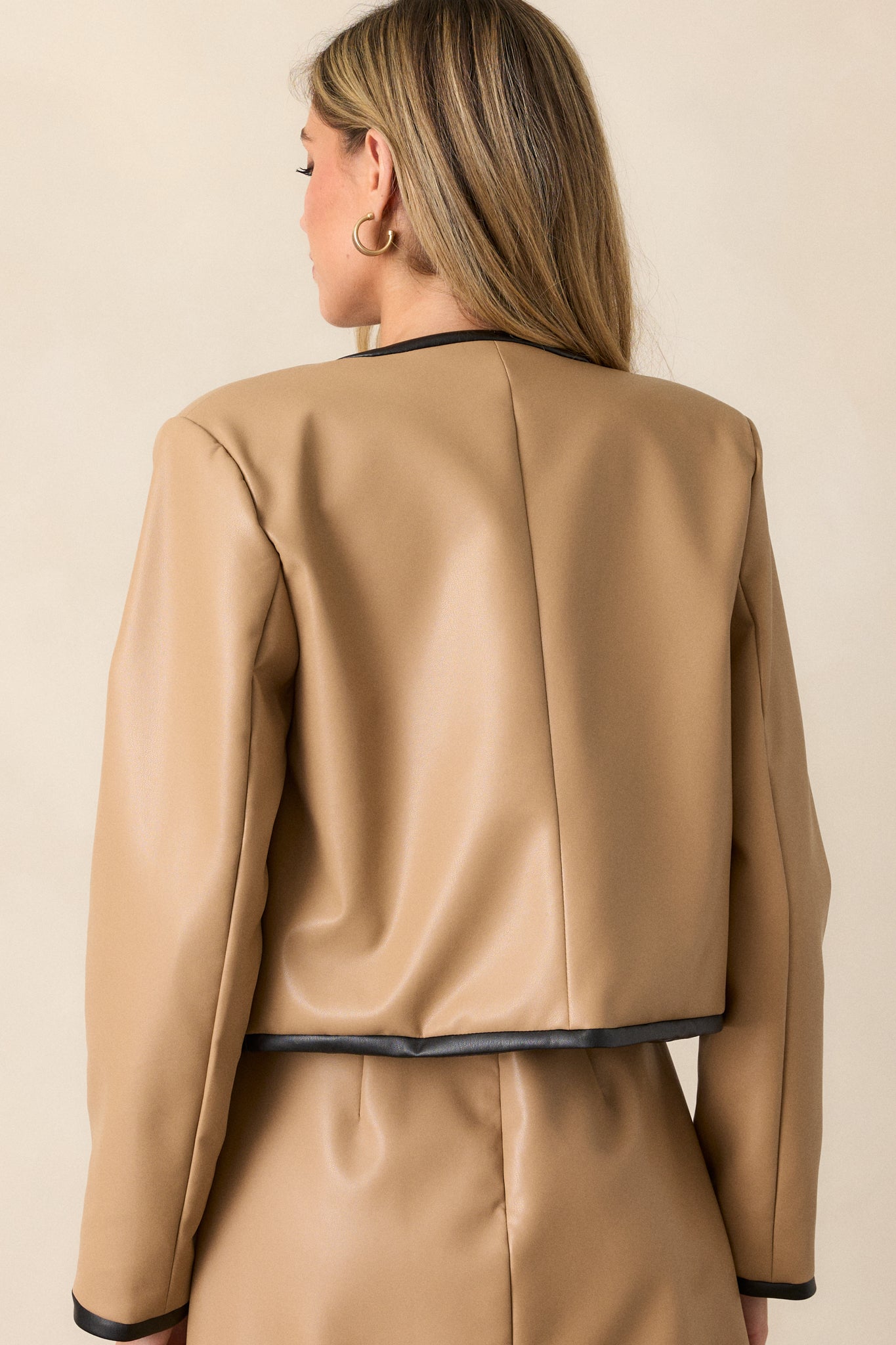 View of the back of the jacket, featuring the continuous camel faux leather design, black trim along the seams, and the overall sleek, structured look from behind.