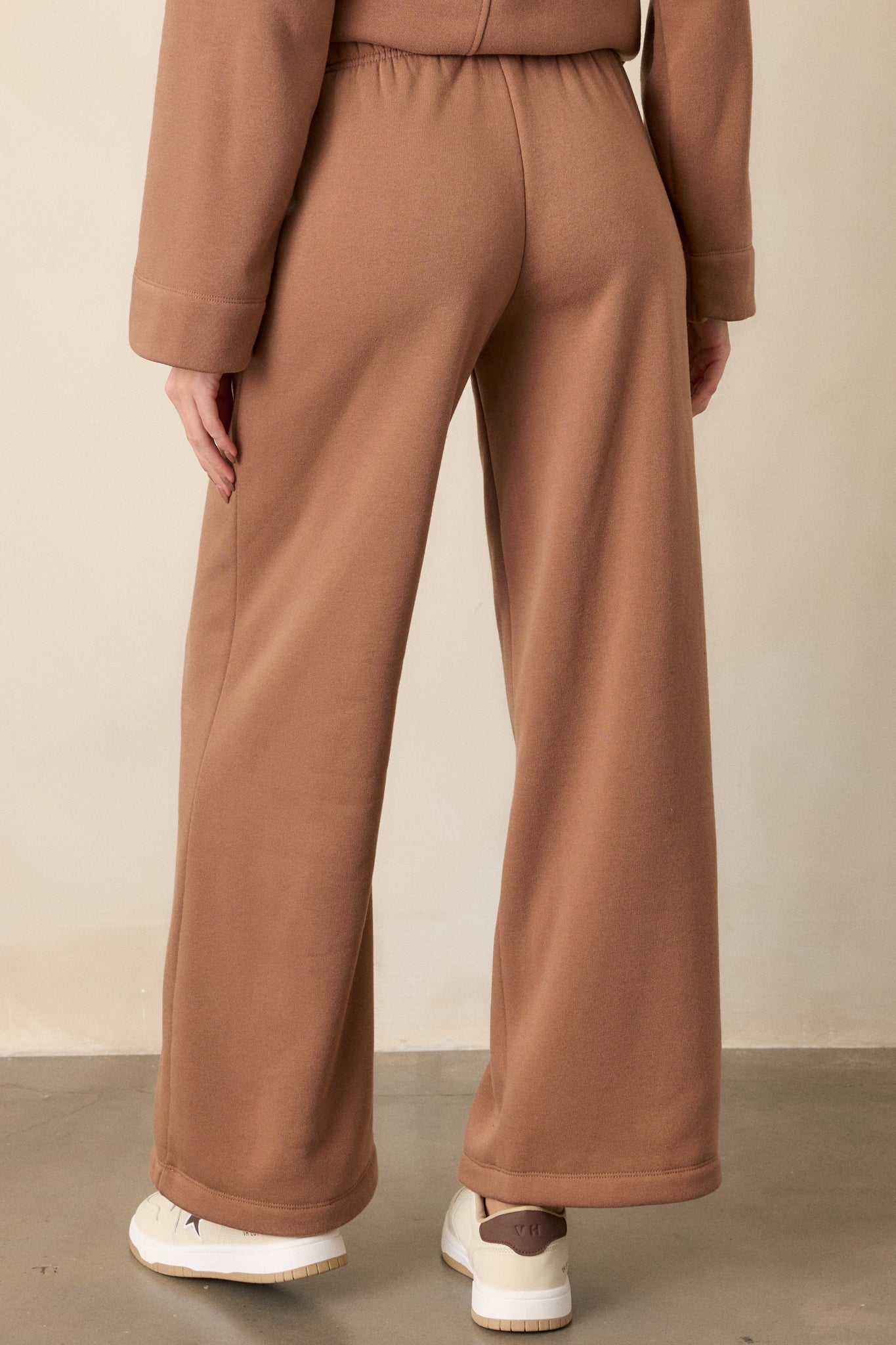 The back view of the brown sweatpants, highlighting the wide-leg fit and smooth fabric at the waistband.