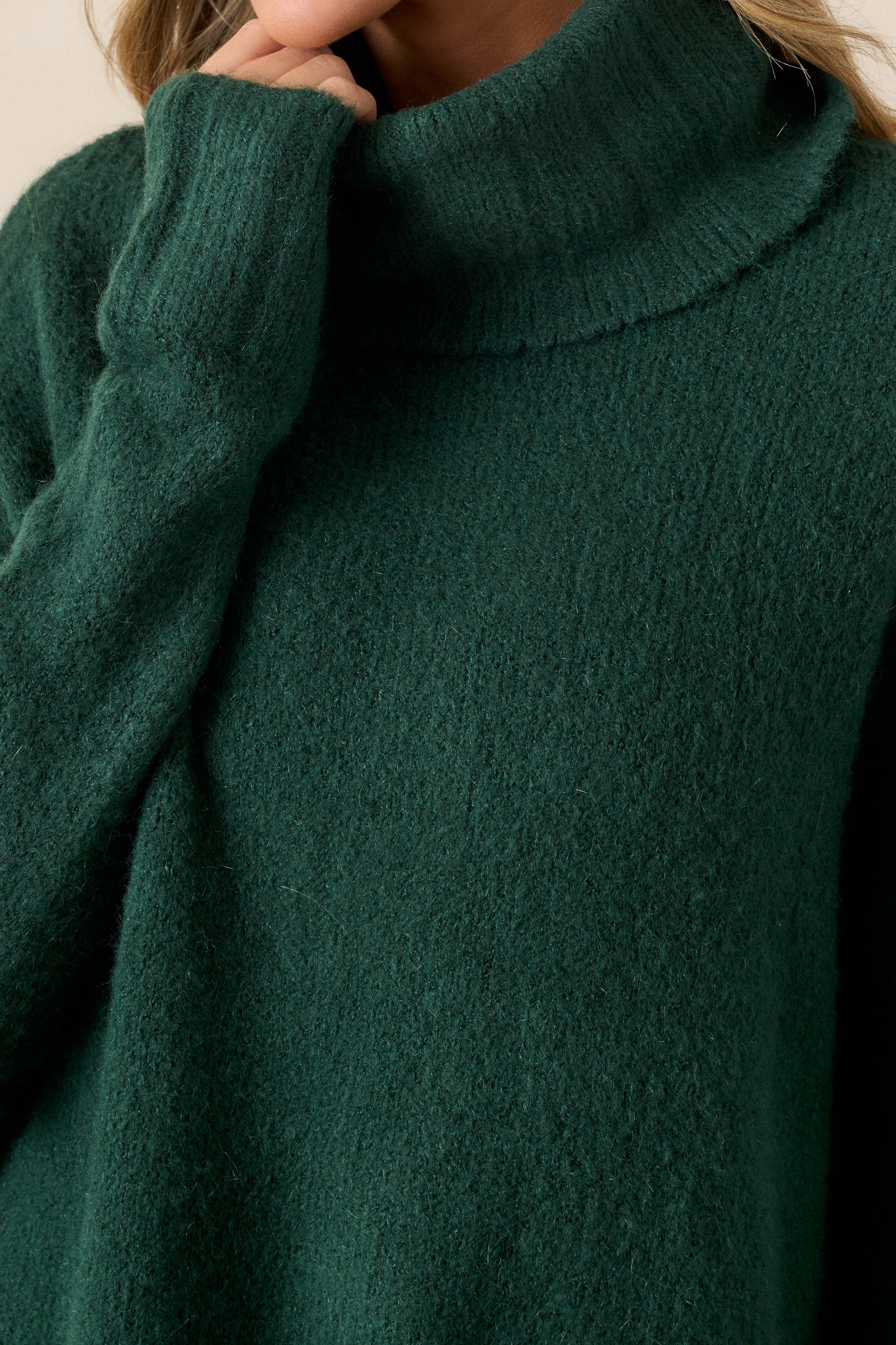 Close up view of this sweater that features a very light eyelash knit design, a turtle cowl neckline, extremely dropped shoulders, and a slight high low hemline.