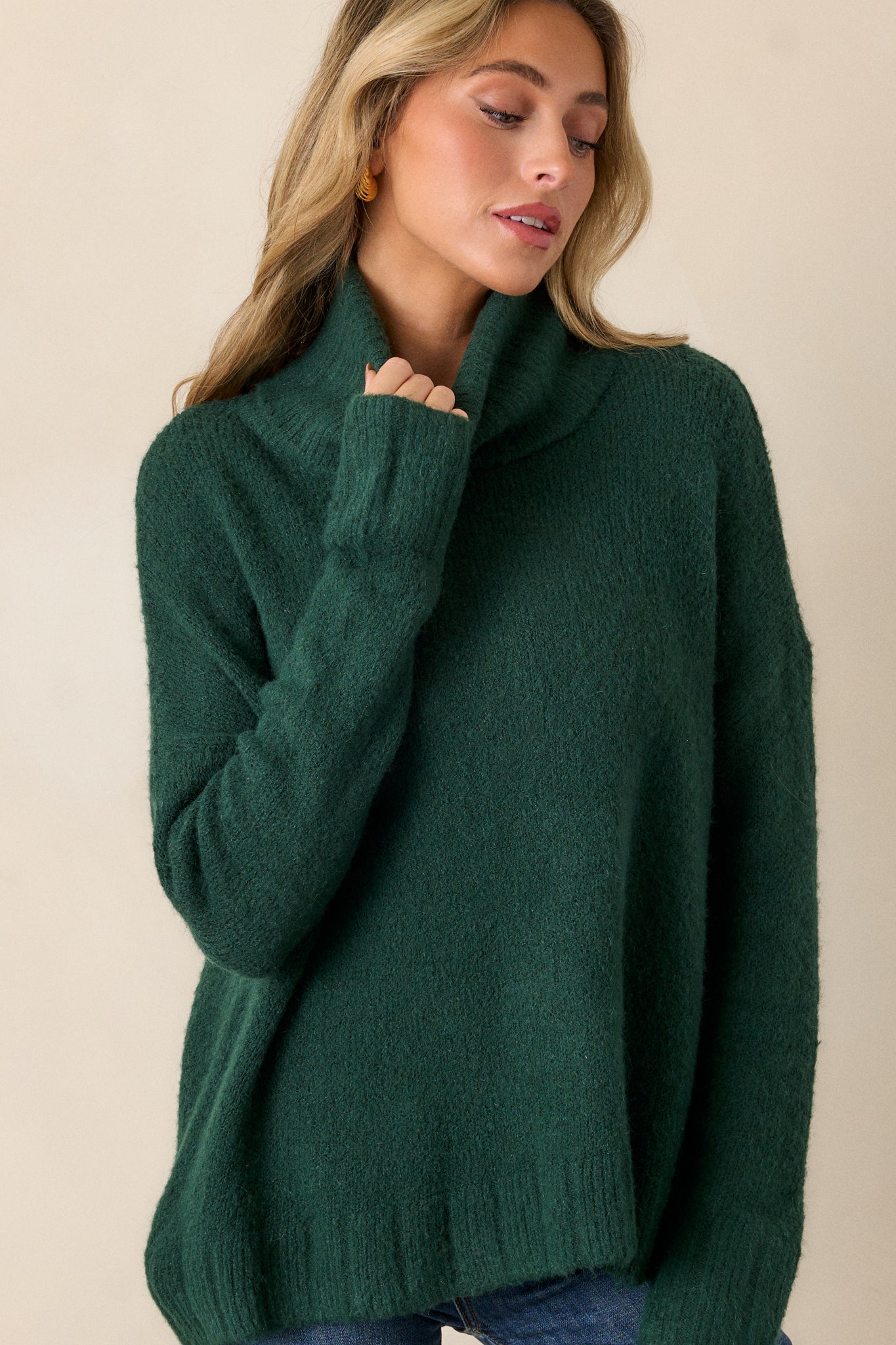 Front view of this hunter green sweater that features a very light eyelash knit design, a turtle cowl neckline, extremely dropped shoulders, and a slight high low hemline.