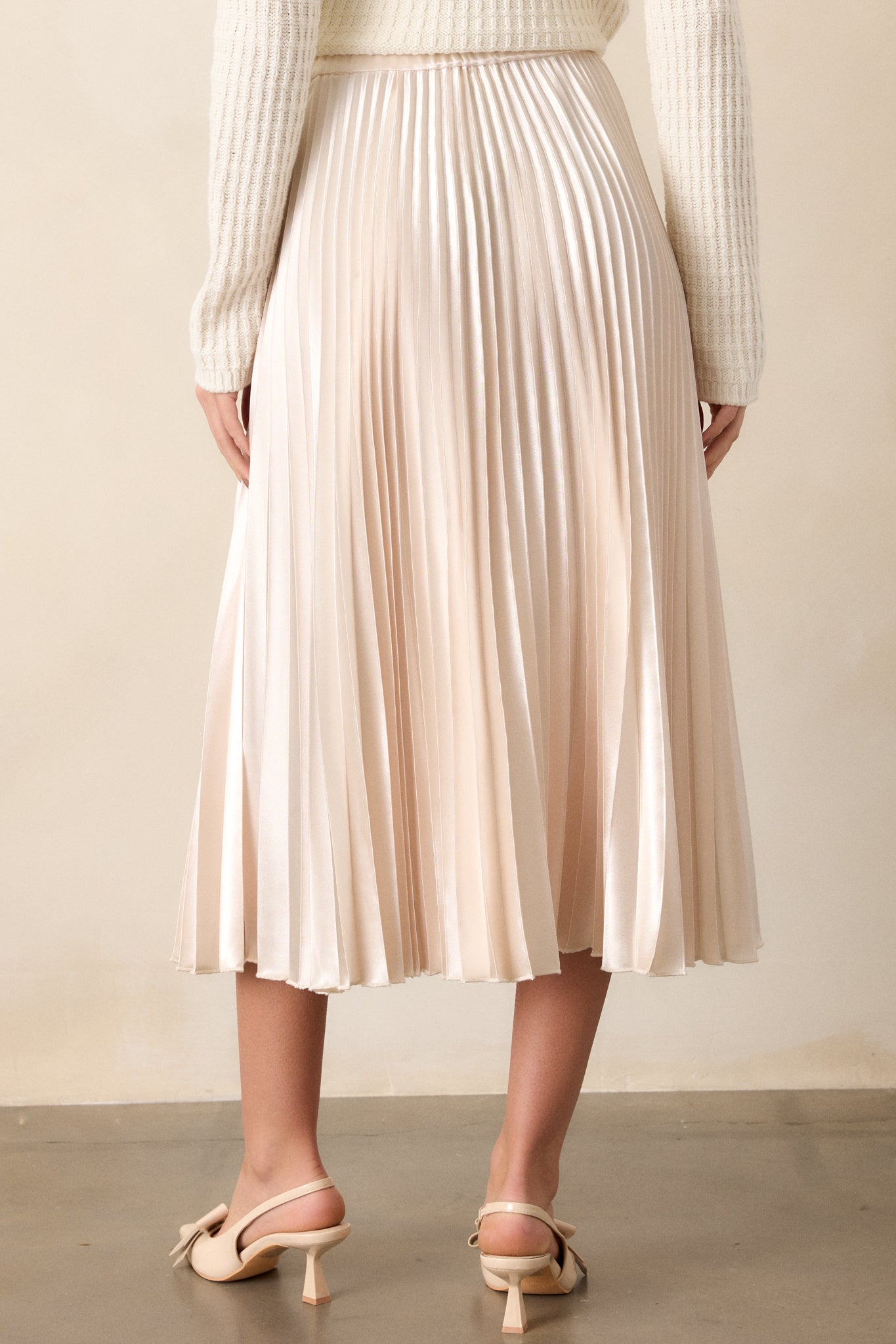 Back view of an ivory midi skirt featuring an elastic insert at the back of the waist, a high waisted design, and heavy pleating throughout.