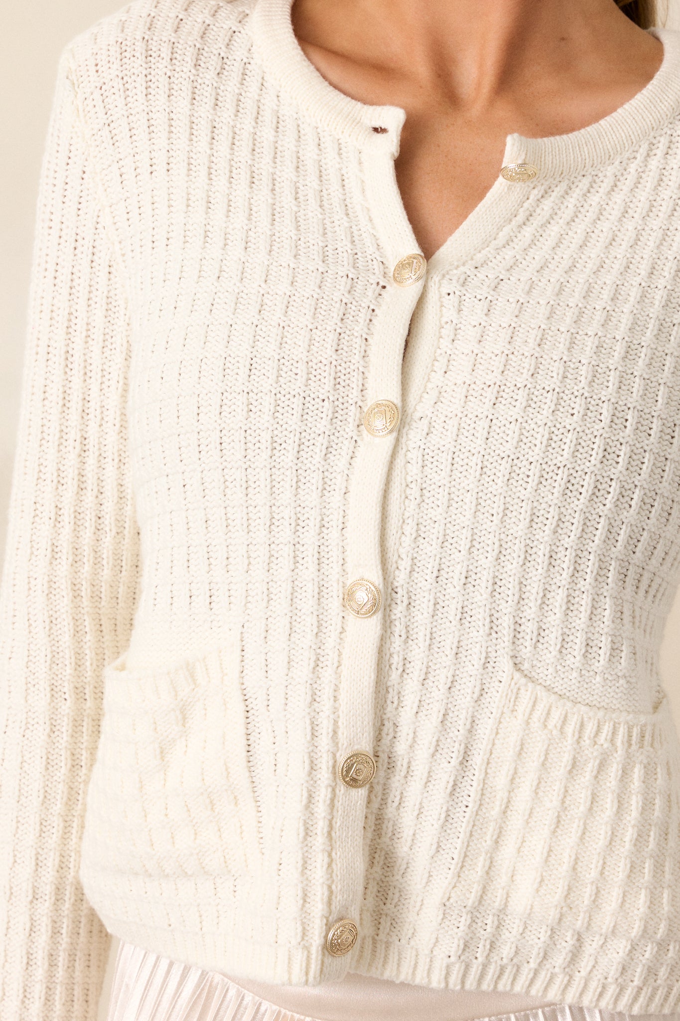 Close-up of the ivory sweater focusing on the gold hardware and the ribbed texture, along with a clear view of the front functional pockets.