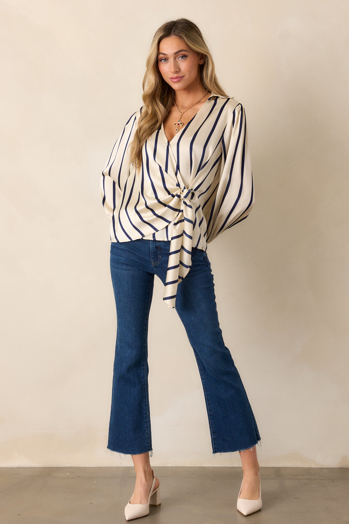 Full view of the ivory blouse with a vertical navy striped pattern, showing its collared v-neckline and wrap tie detail at the waist.