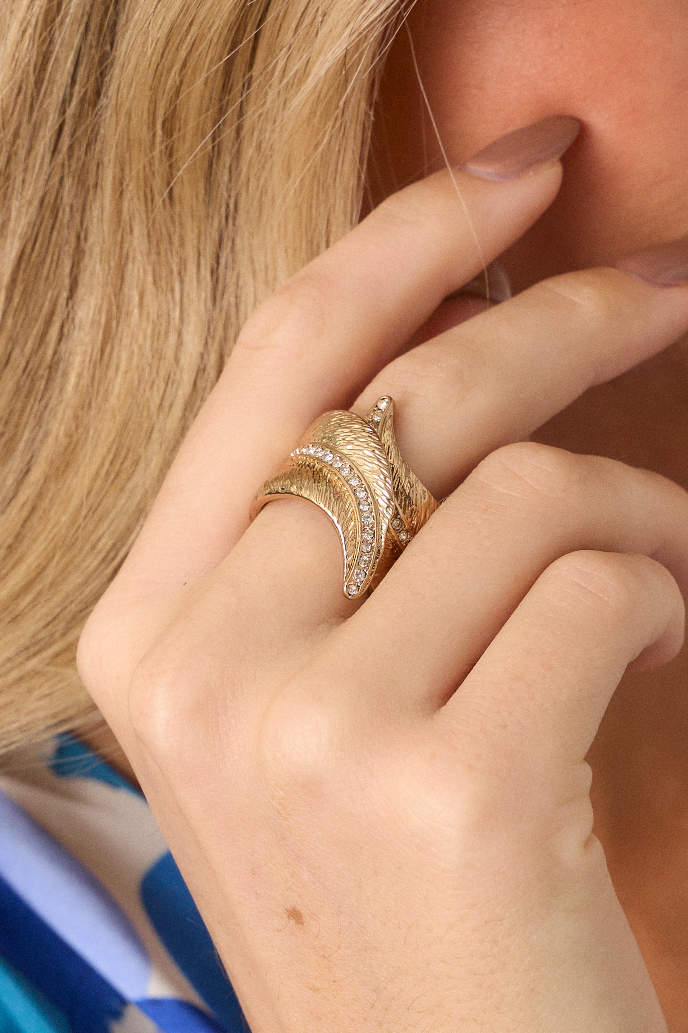 Front view of a gold ring featuring textured gold hardware, a split band, a feathered design, a line of rhinestones through the middle of the ring to the tips of the feathers.