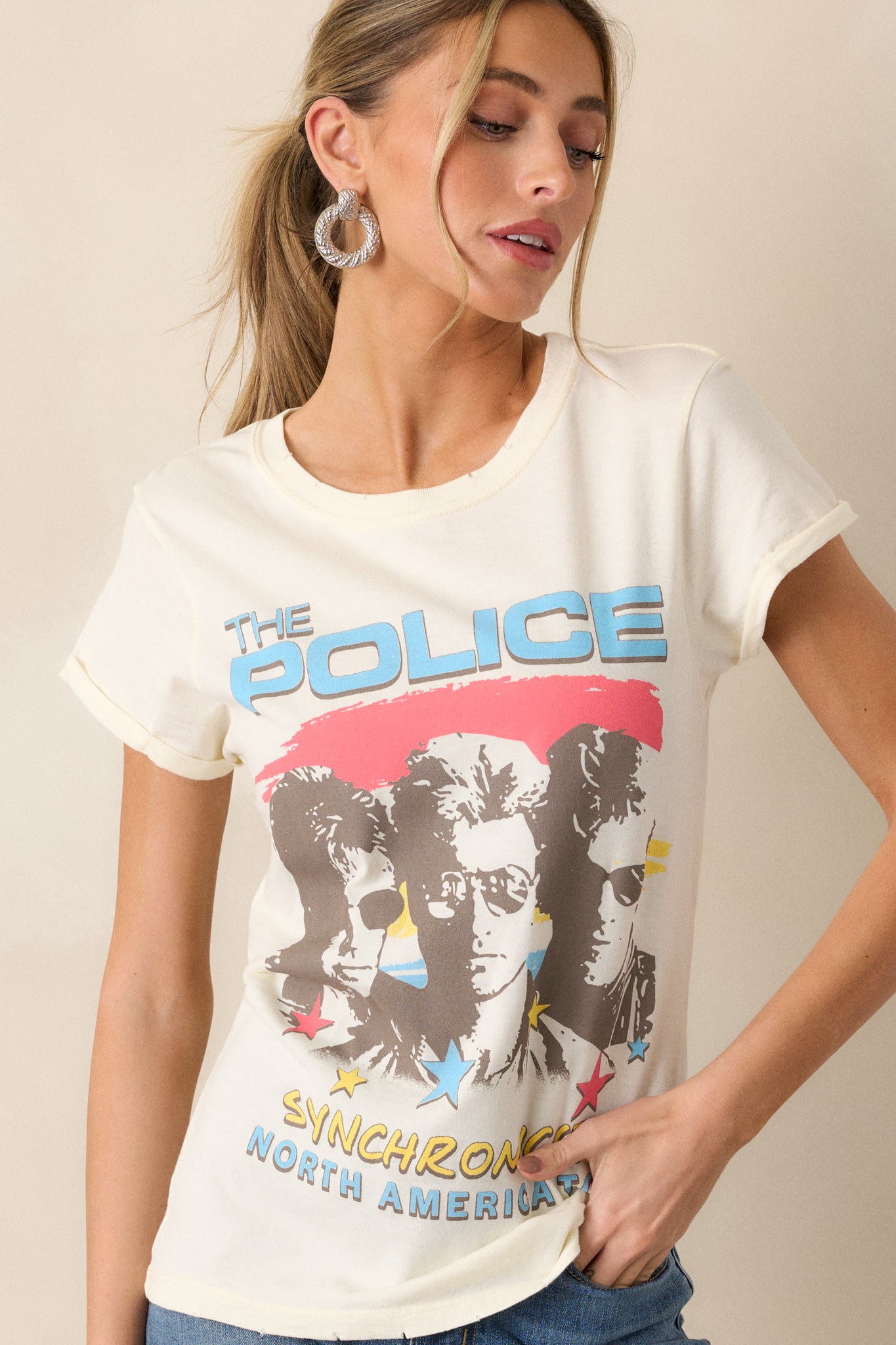 A front view of the ivory tee featuring a round neckline, cuffed sleeves, and a distressed hem. The graphic on the front reads "The Police Synchronicity North America Tour," showcasing the relaxed fit of the top.