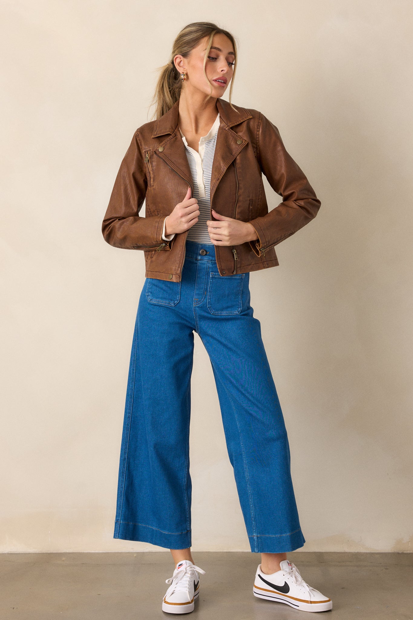 Full length view of a jacket with washed gold hardware, a collar neckline with snap buttons, a front functional zipper, three functional zipper pockets, and slits on the sleeves with zipper closures.