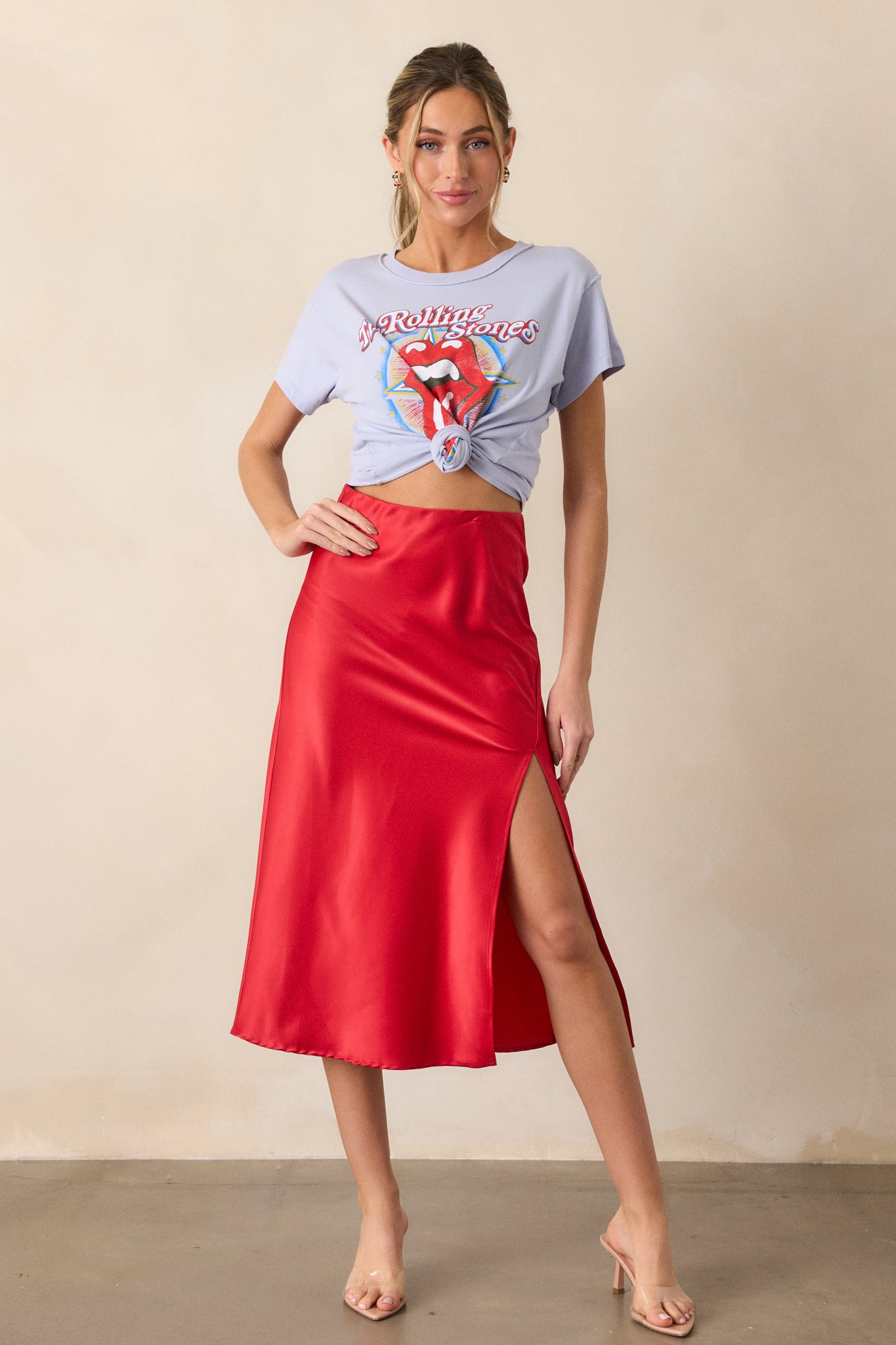 Full length shot showcasing the red satin skirt, featuring a high waisted design with an elastic waistband, a slit up the leg, and a smooth satin finish.