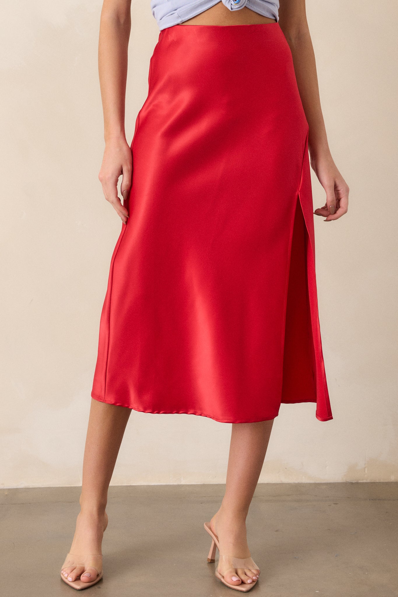 Complete front profile of the red satin skirt, highlighting the slit up the leg and the high waistline, with the satin fabric flowing elegantly.