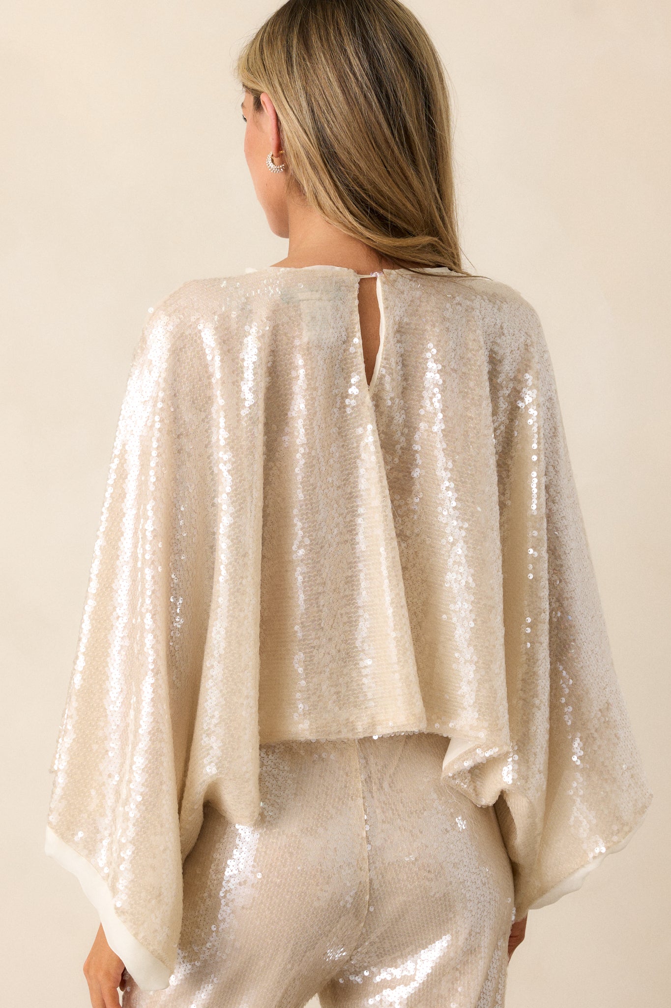 View of the back of the top, featuring the continuous sequin design, the relaxed dolman sleeves, and the cropped hemline from behind.