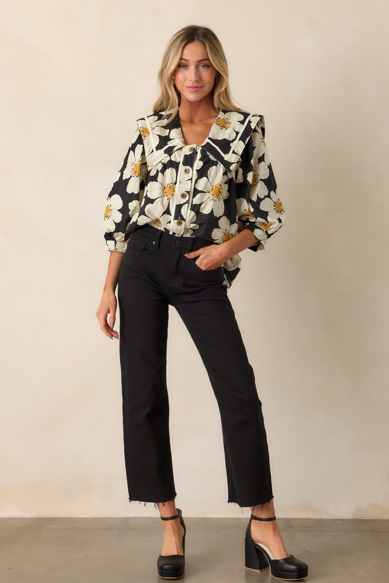 A front view of the black blouse, highlighting the ivory floral print, functional button front with worn gold flower buttons, and peter pan collar neckline.