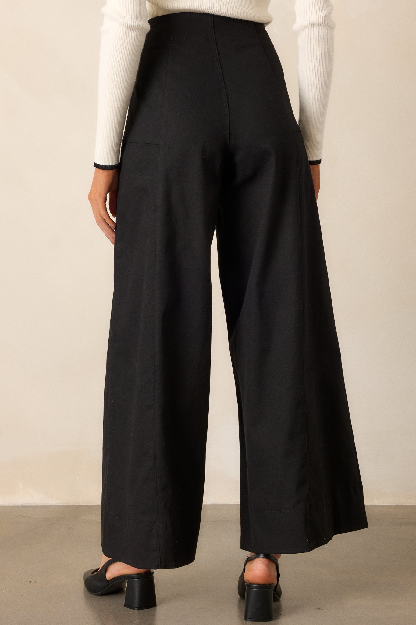 A back view of the black pants, highlighting the smooth finish, high-waisted fit, and wide-leg silhouette.