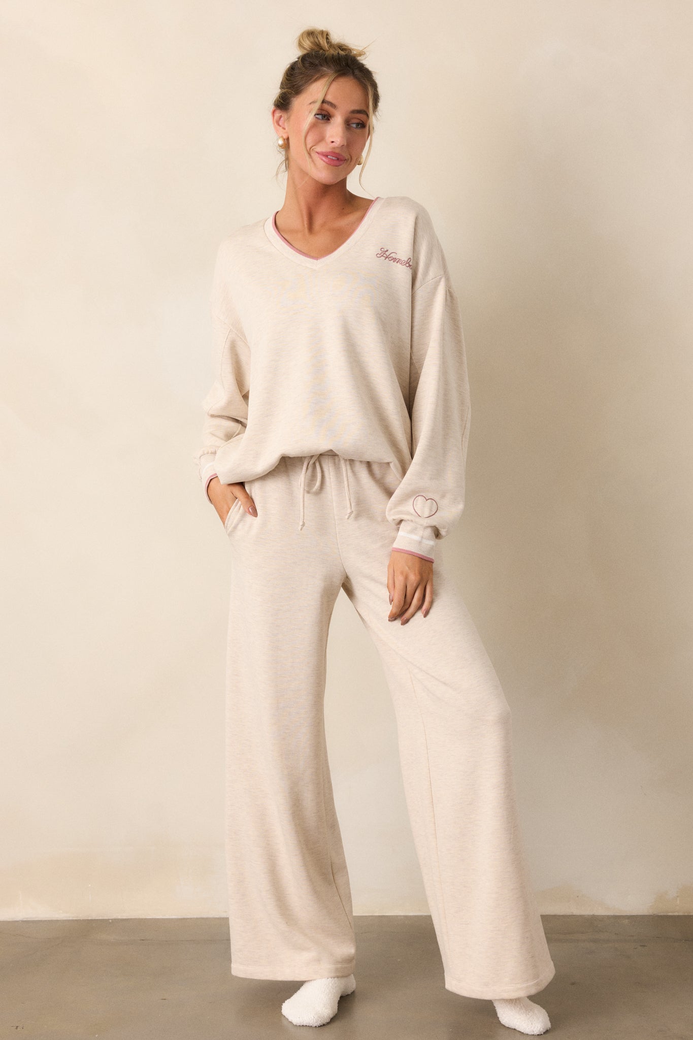 A full-length shot of the top of the oatmeal sweatshirt, showcasing the v-neckline with pink trim detailing and the "Homebody" embroidery on the upper left bust.