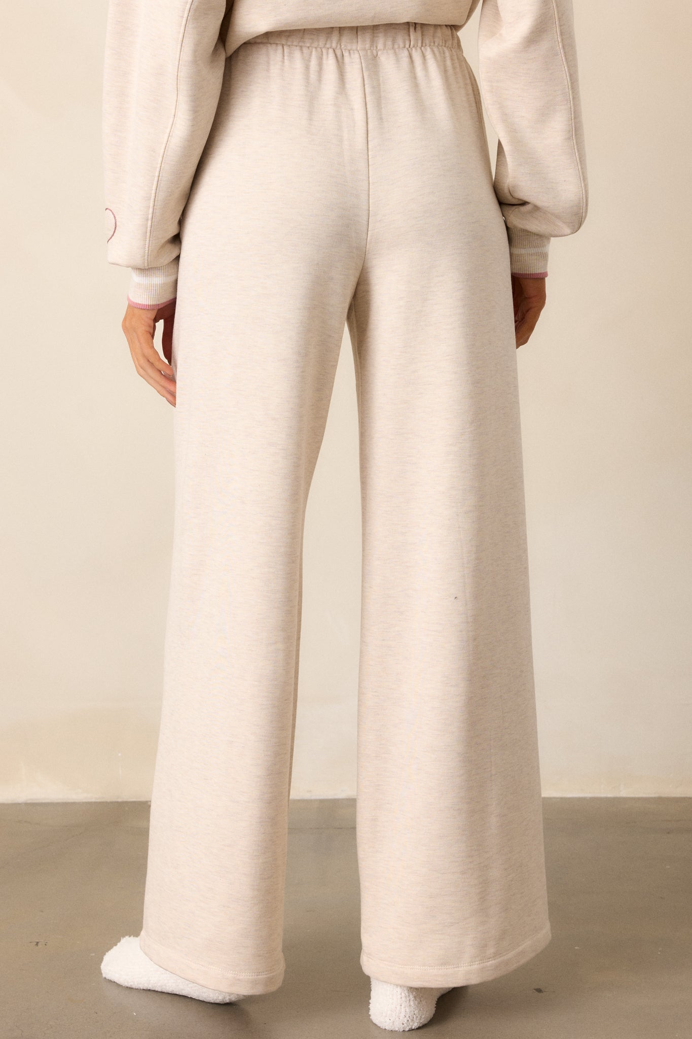 A back view of the oatmeal pants, highlighting the wide leg fit and the soft fleece material. The waistband and functional pockets are clearly visible from behind.