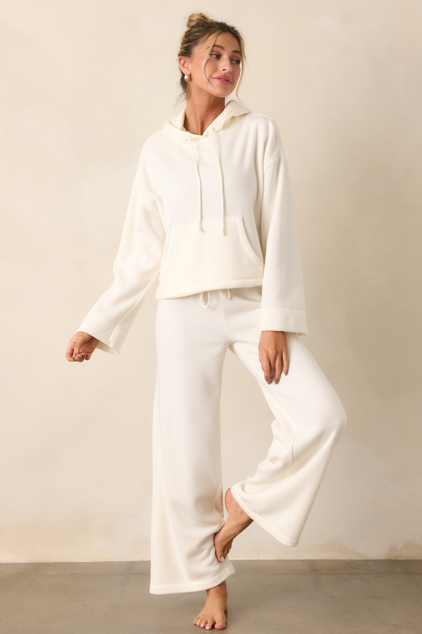 Full body image of the ivory sweatshirt, highlighting the loose long sleeves, hooded neckline, and roomy kangaroo pocket.