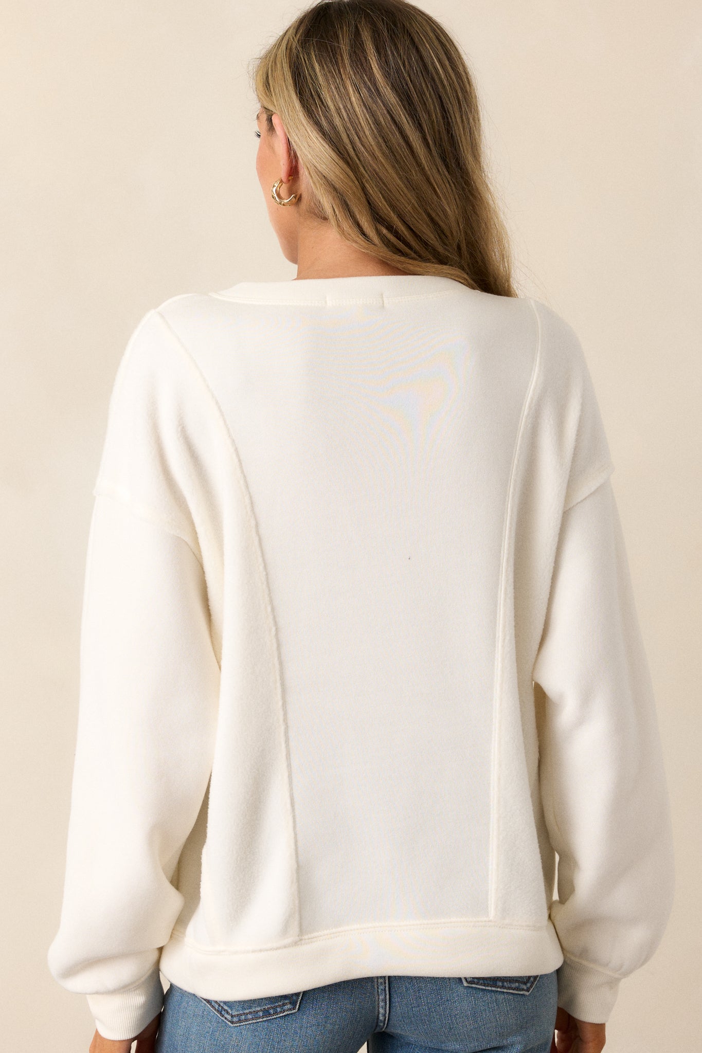 Back view of the ivory sweatshirt, highlighting the relaxed fit and continuation of the subtle reverse paneling details on the back.