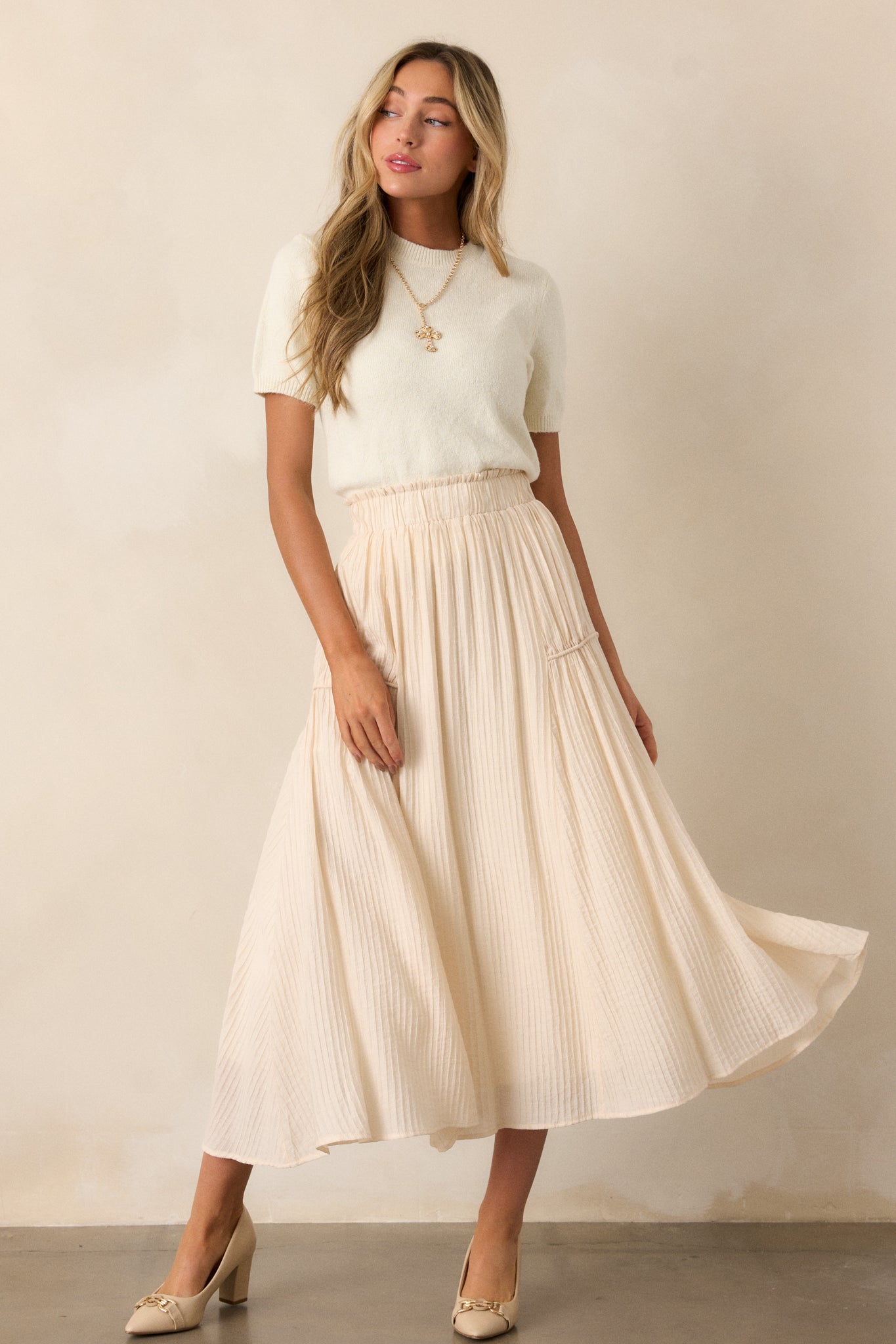 Action shot of a beige maxi skirt displaying the fit and movement, highlighting the high waist design, elastic waistband, ribbed texture, and flowing silhouette.