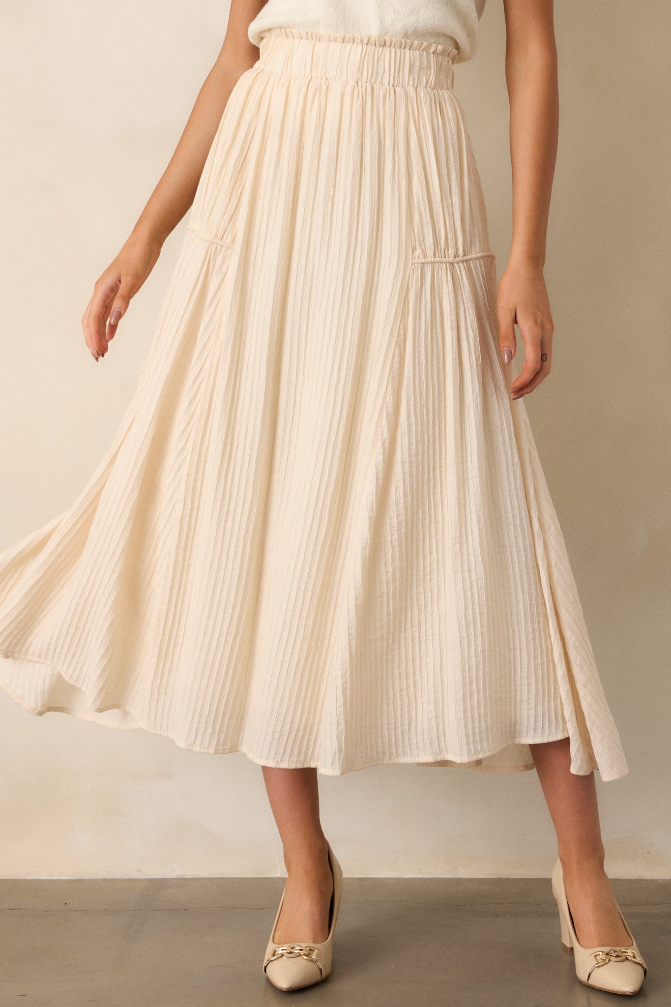 Front angled view of a beige maxi skirt featuring a high waist design, an elastic waistband, a ribbed texture, and a flowing silhouette