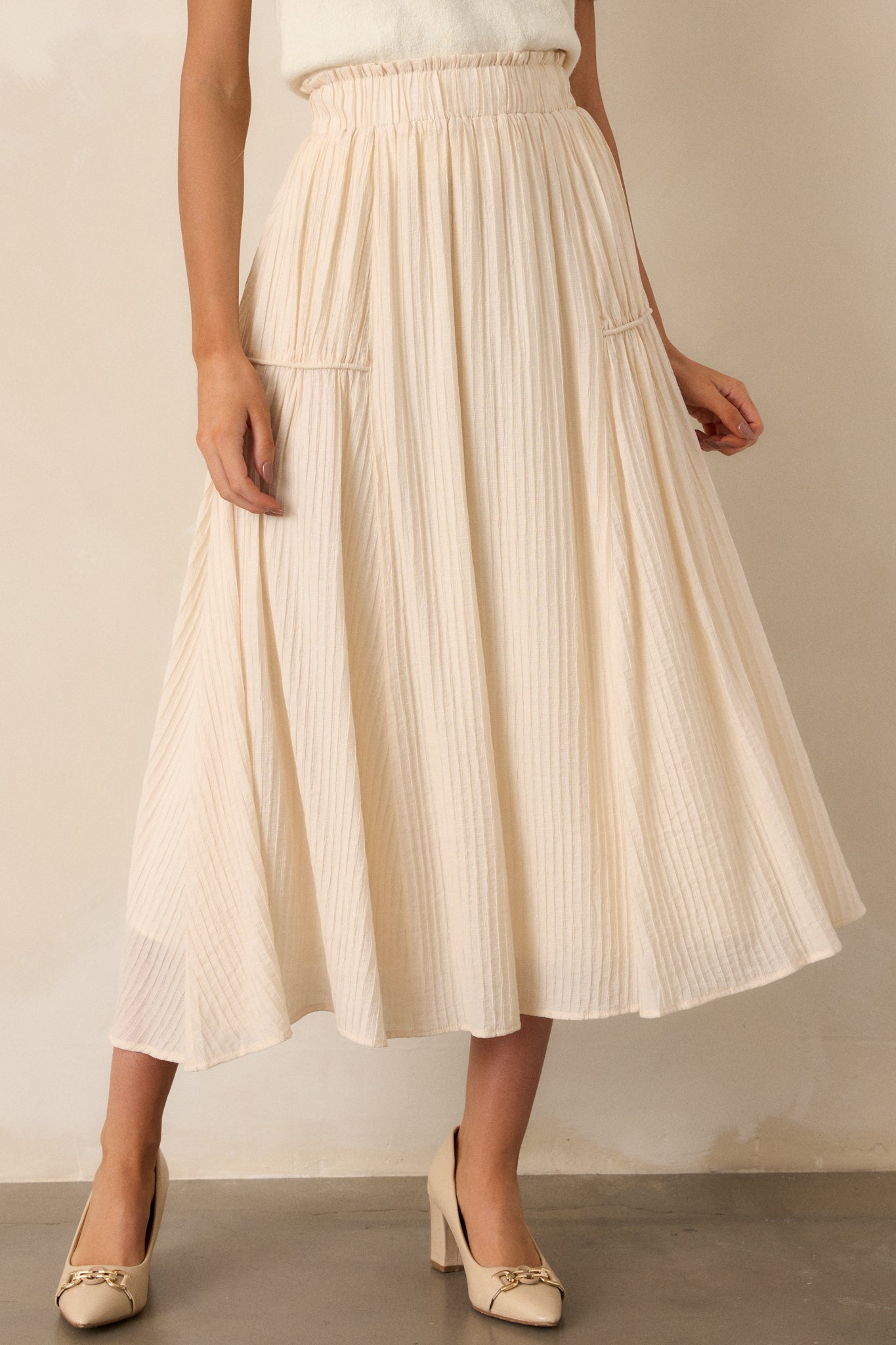 Front view of a beige maxi skirt featuring a high waist design, an elastic waistband, a ribbed texture, and a flowing silhouette.