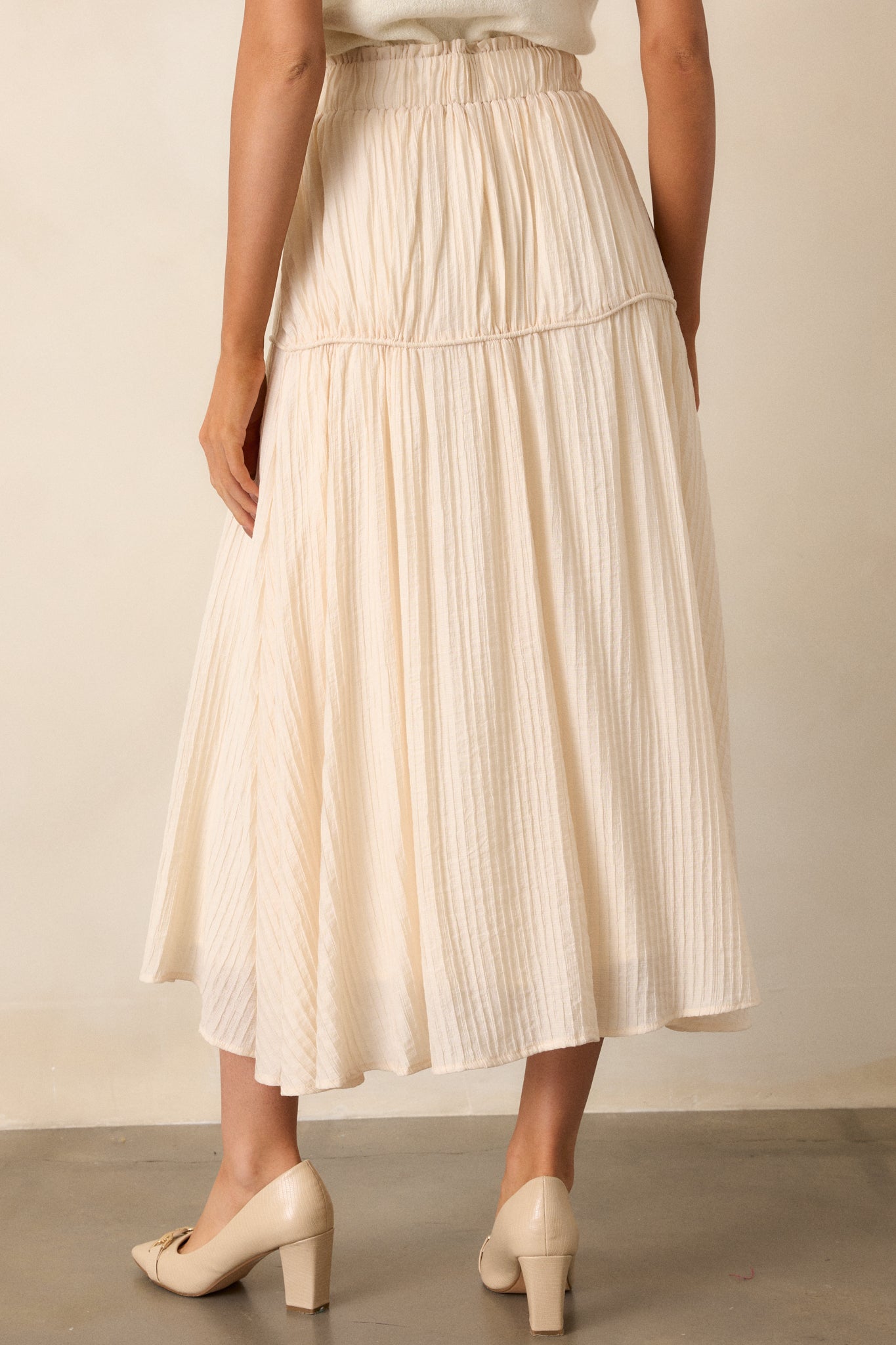 Back view of a beige maxi skirt highlighting the high waist design, elastic waistband, and ribbed texture.