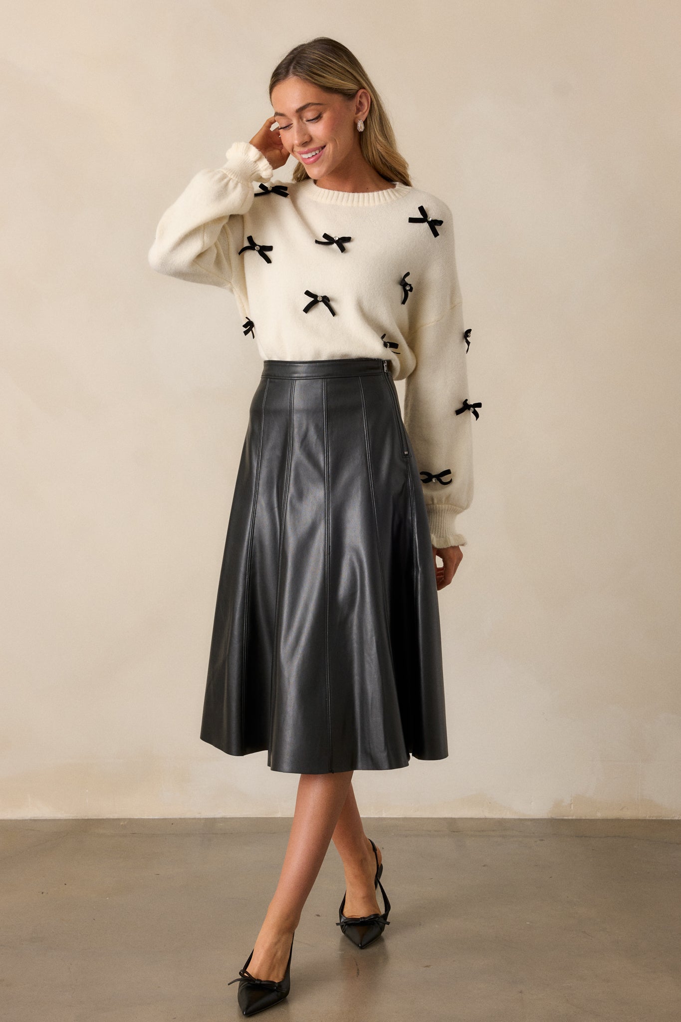 Front view of the ivory sweater, showcasing the ribbed crew neckline, cuffed long sleeves, and scattered black velvet bows with rhinestone centers.