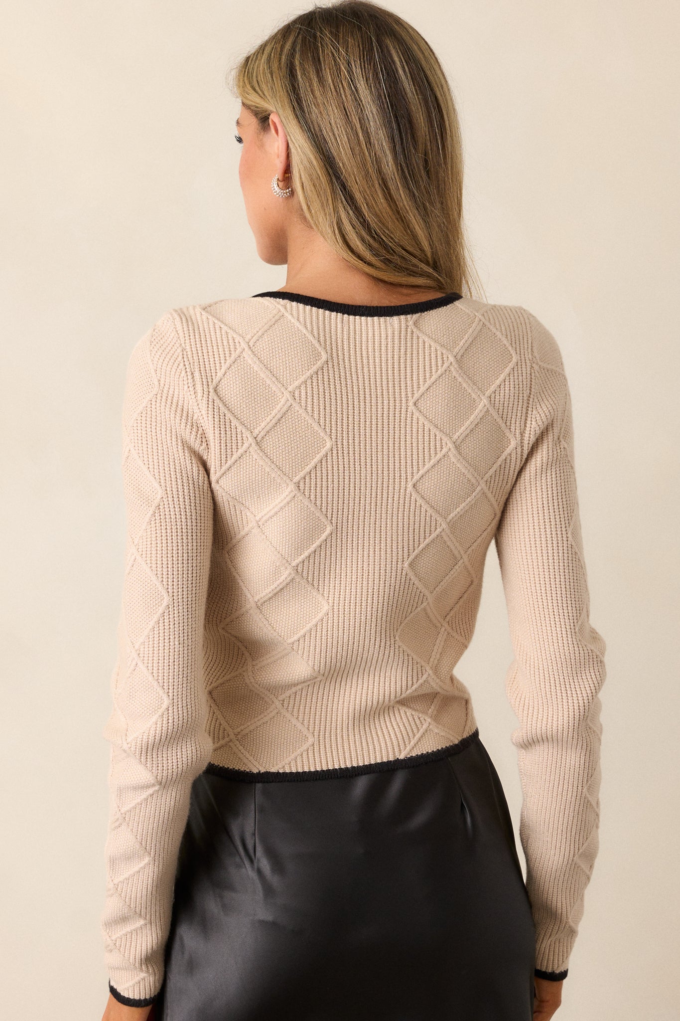 Back view of this beige sweater that features a v-neckline, a faux button front, black bow embellishments, faux pearl and rhinestone detailing, soft knit material, a black trim, long sleeves, and a cropped length.