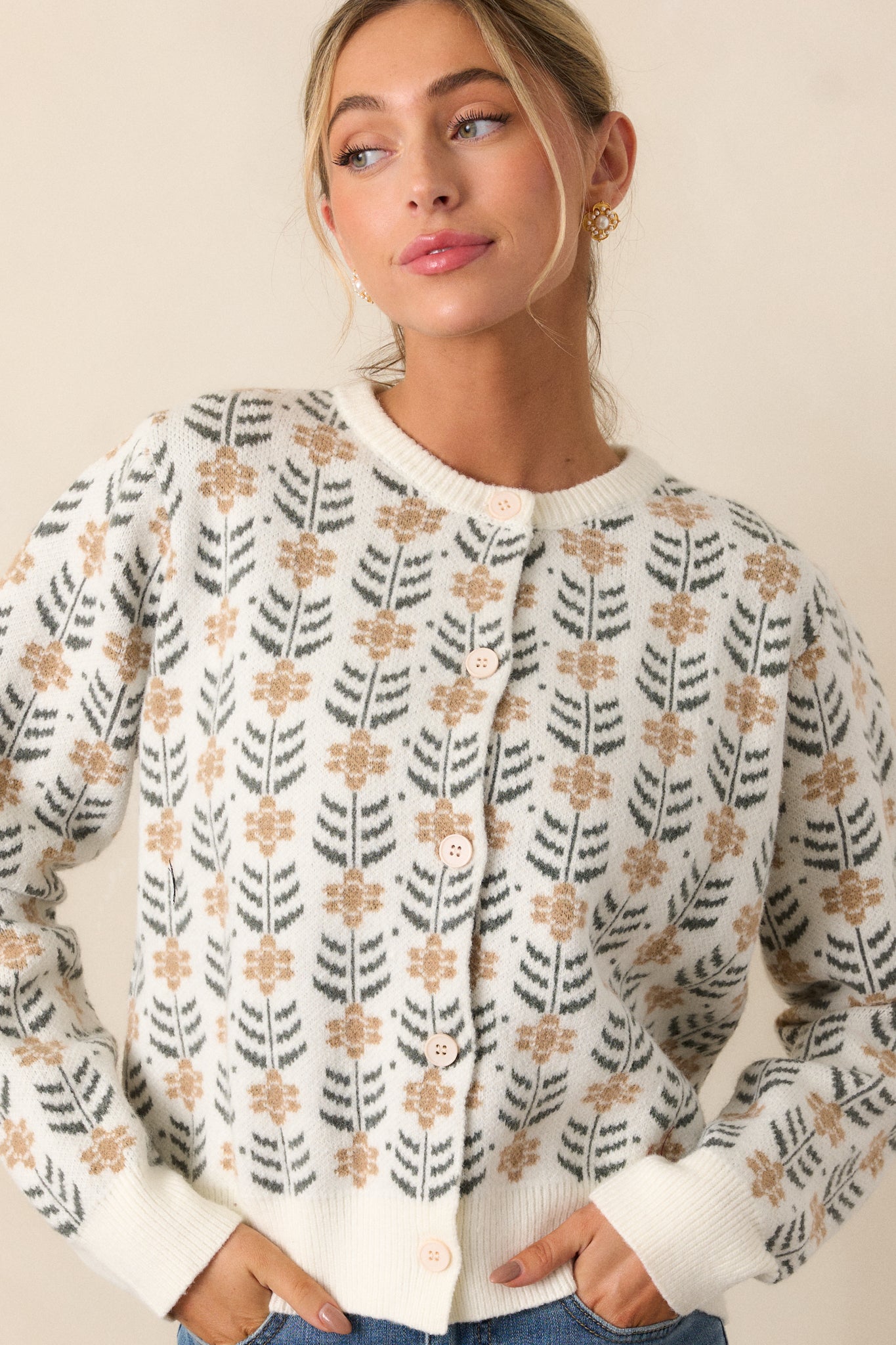 Front button up view of an ivory cardigan featuring a round neckline, a repeating pattern of delicate beige floral motifs with dark green leaf accents, ribbed hems and long sleeves.