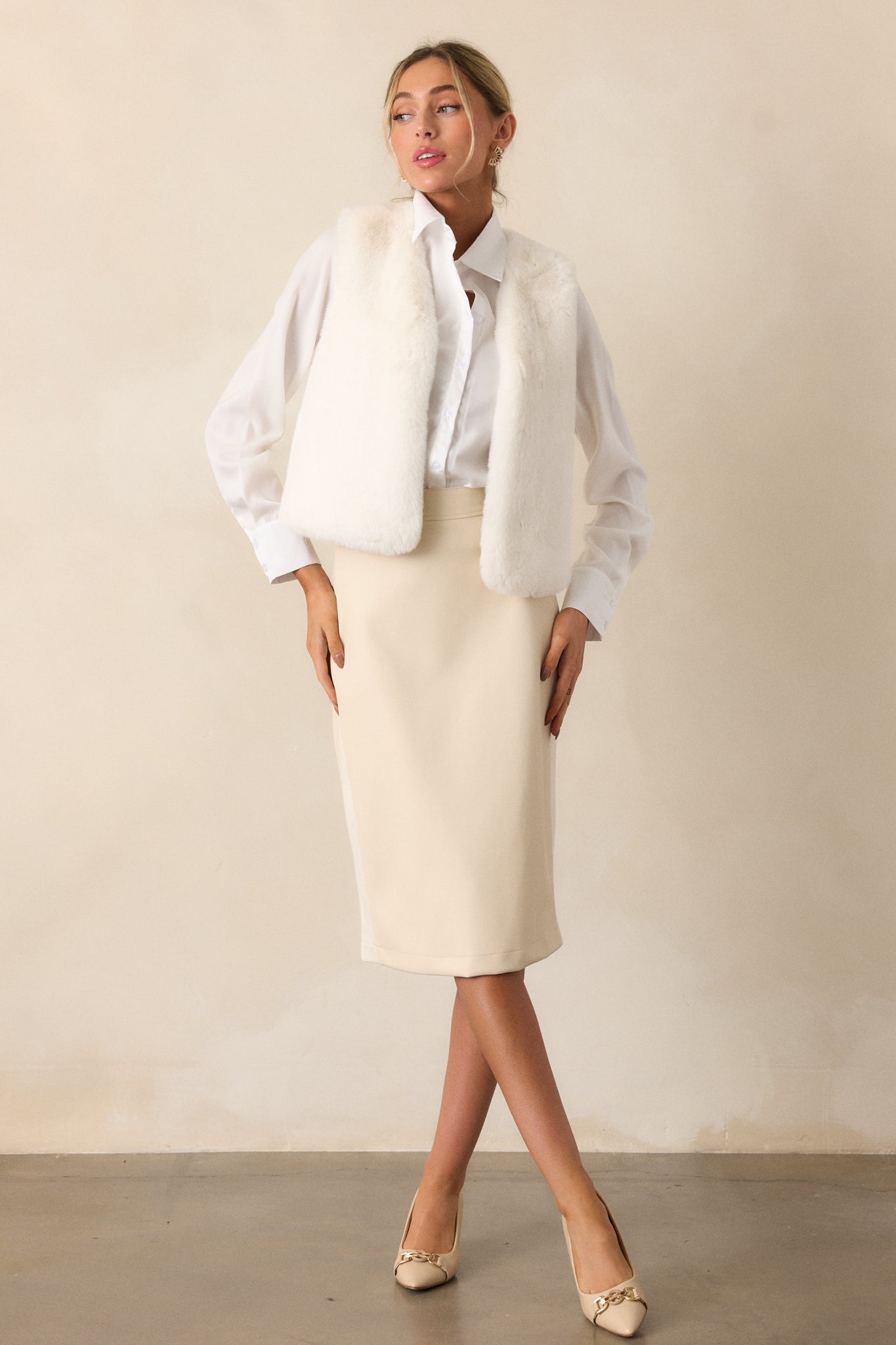 Full body view of an ivory skirt featuring a fitted design, midi length, faux leather fabric, discrete back zipper and small back slit.