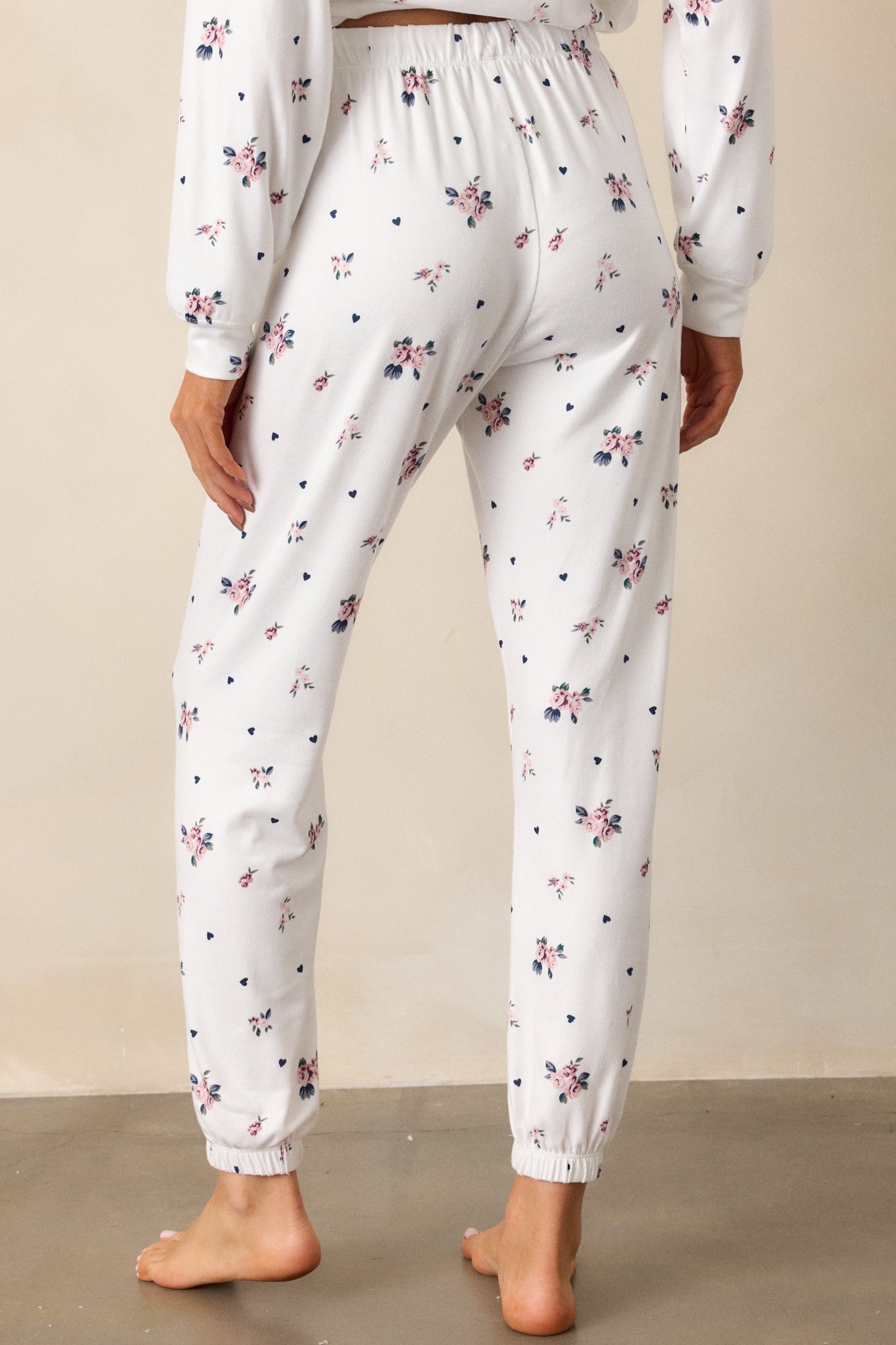 A back view of the ivory joggers highlighting the elastic waistband and high waist design. The rosebud pattern continues on the back, with the elastic ankle cuffs visible at the hem.