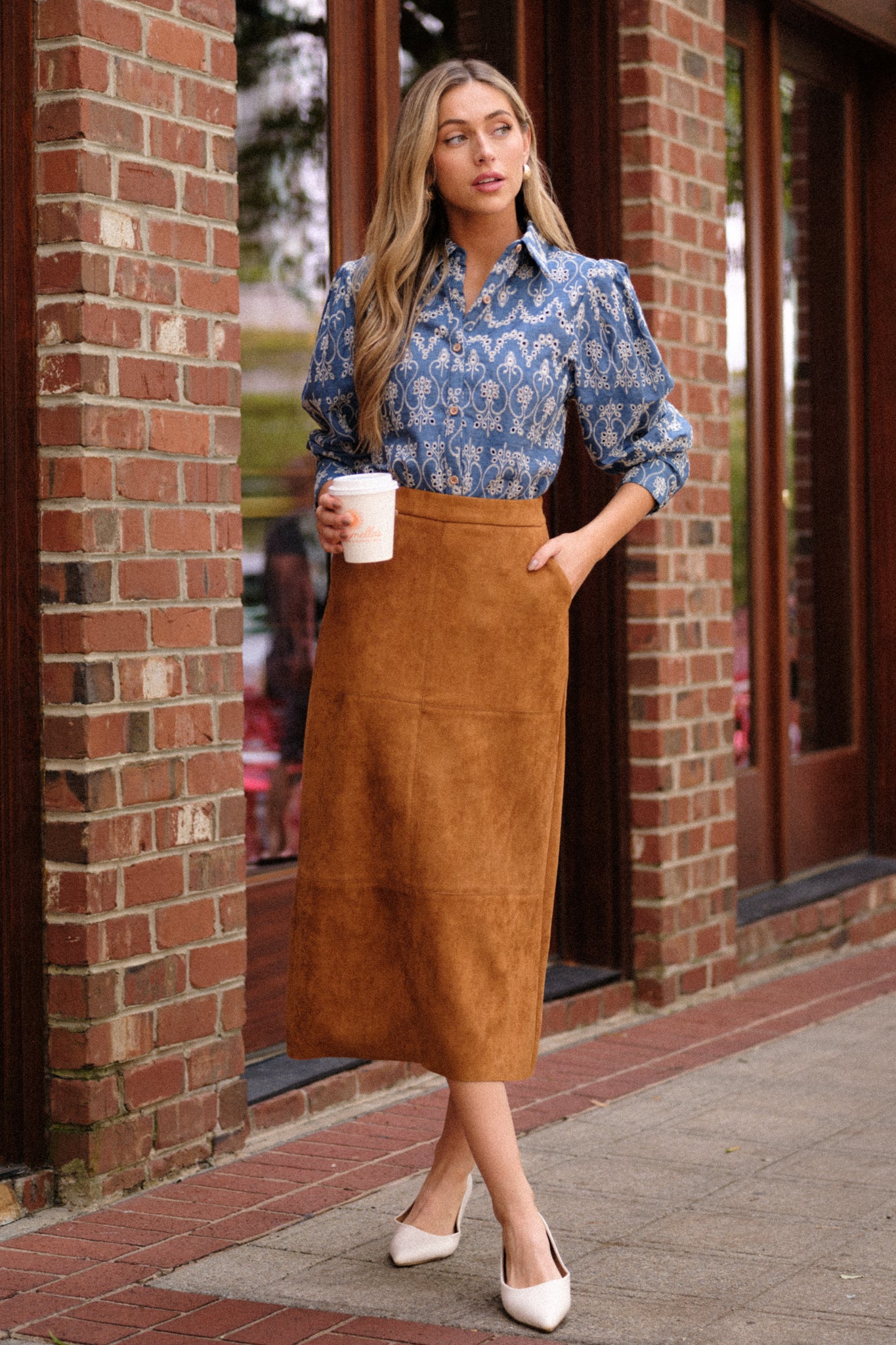 This midi skirt features a caramel brown faux suede material, an A-line silhouette, functional pockets, and a small slit up the back of the skirt.